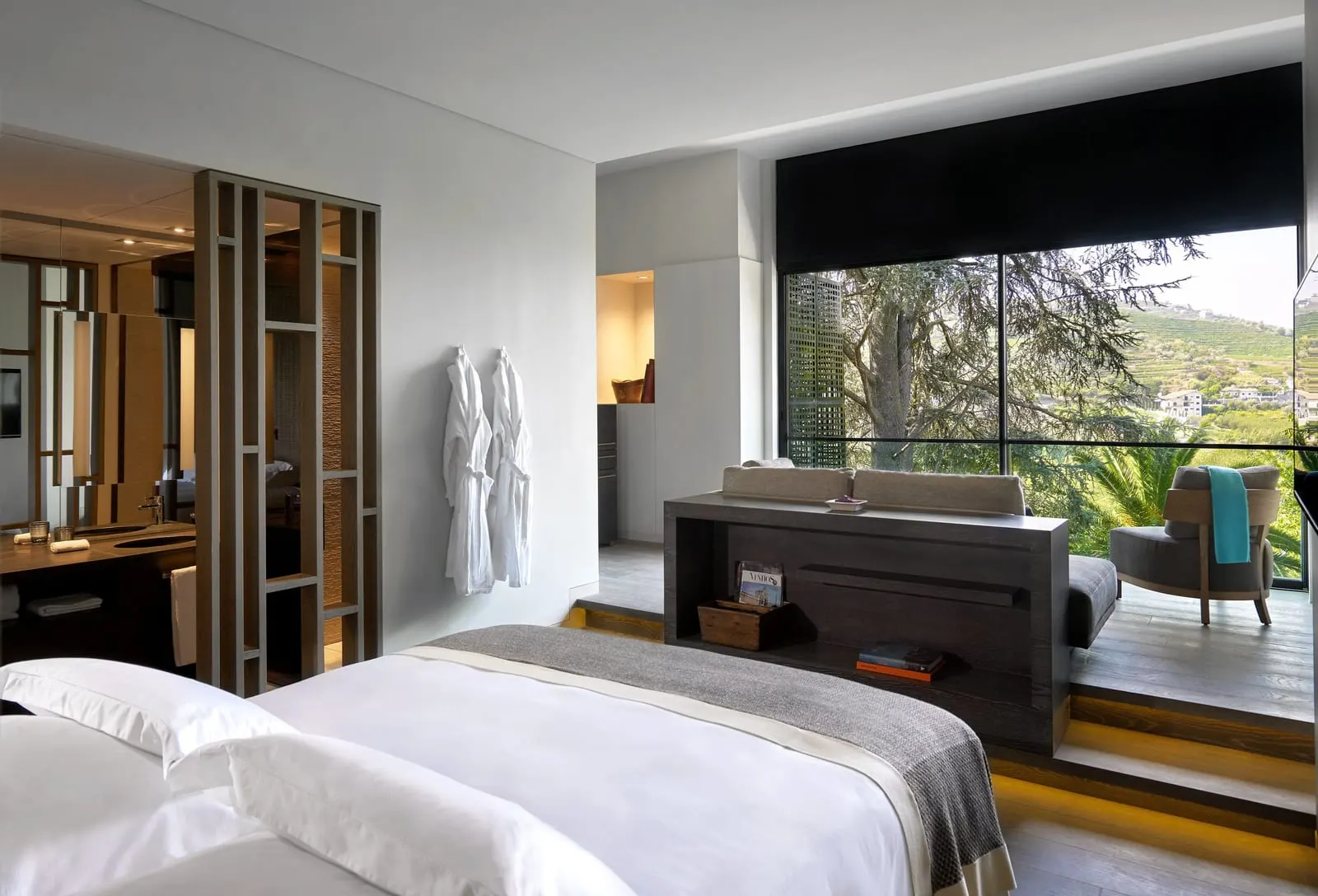 Quinta Deluxe at Six Senses Douro Valley: the bed, a raised sofa nook by a large window onto trees, and a screened bathroom