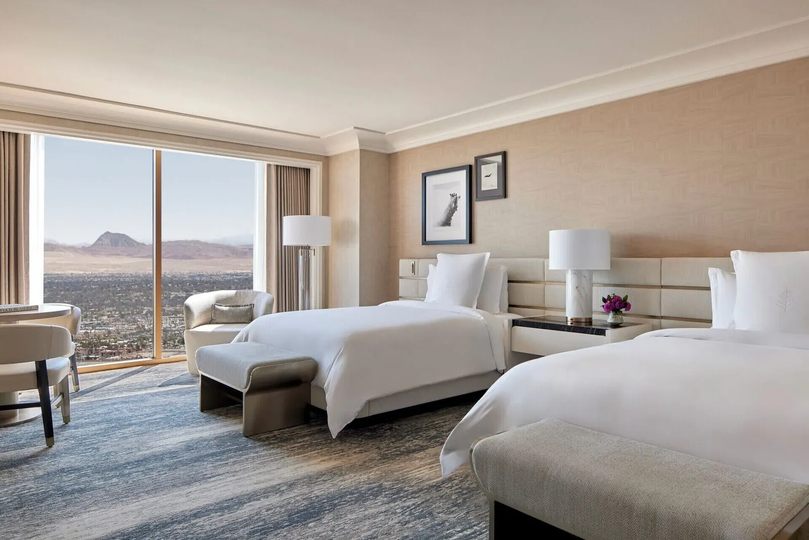 Deluxe Room im Four Seasons Hotel Las Vegas: zwei Queensize-Betten, jeweils mit einer Bank am Fußende, sowie ein Sessel und ein runder Tisch an einem raumhohen Fenster