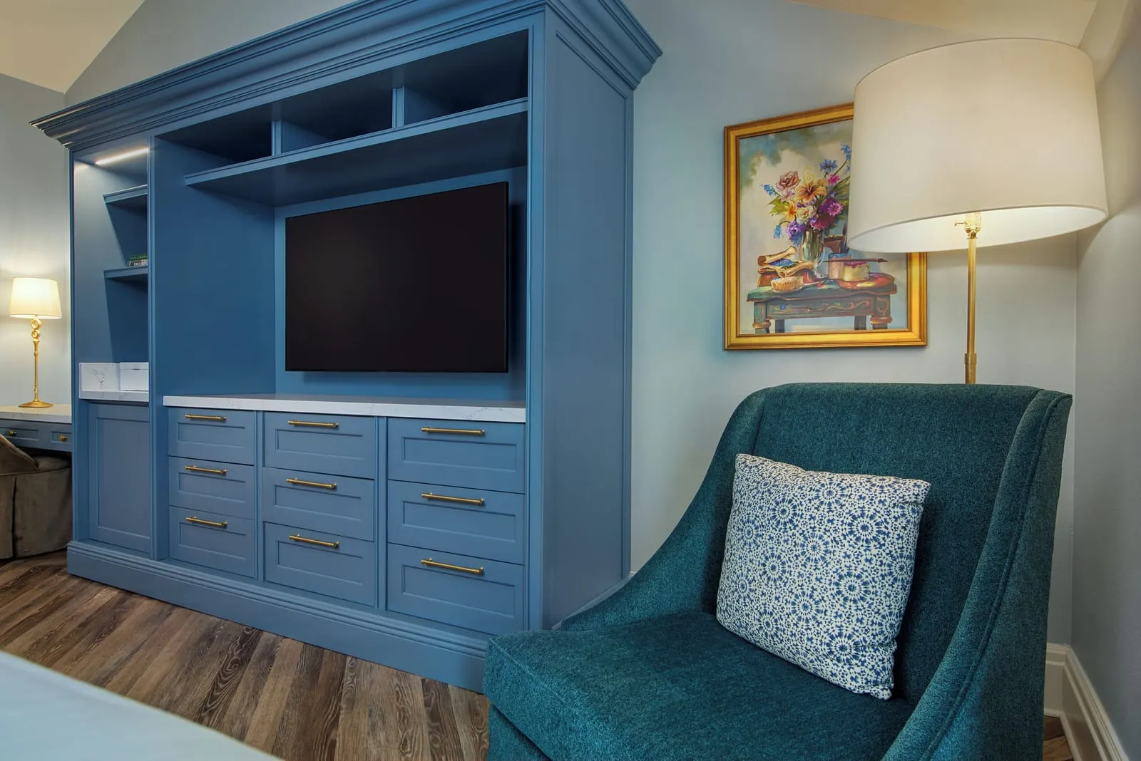 Theme Park View room at Disney's Grand Floridian Resort & Spa: a built-in blue cabinet with a television and drawers, a teal armchair and a floor lamp under a framed flower painting