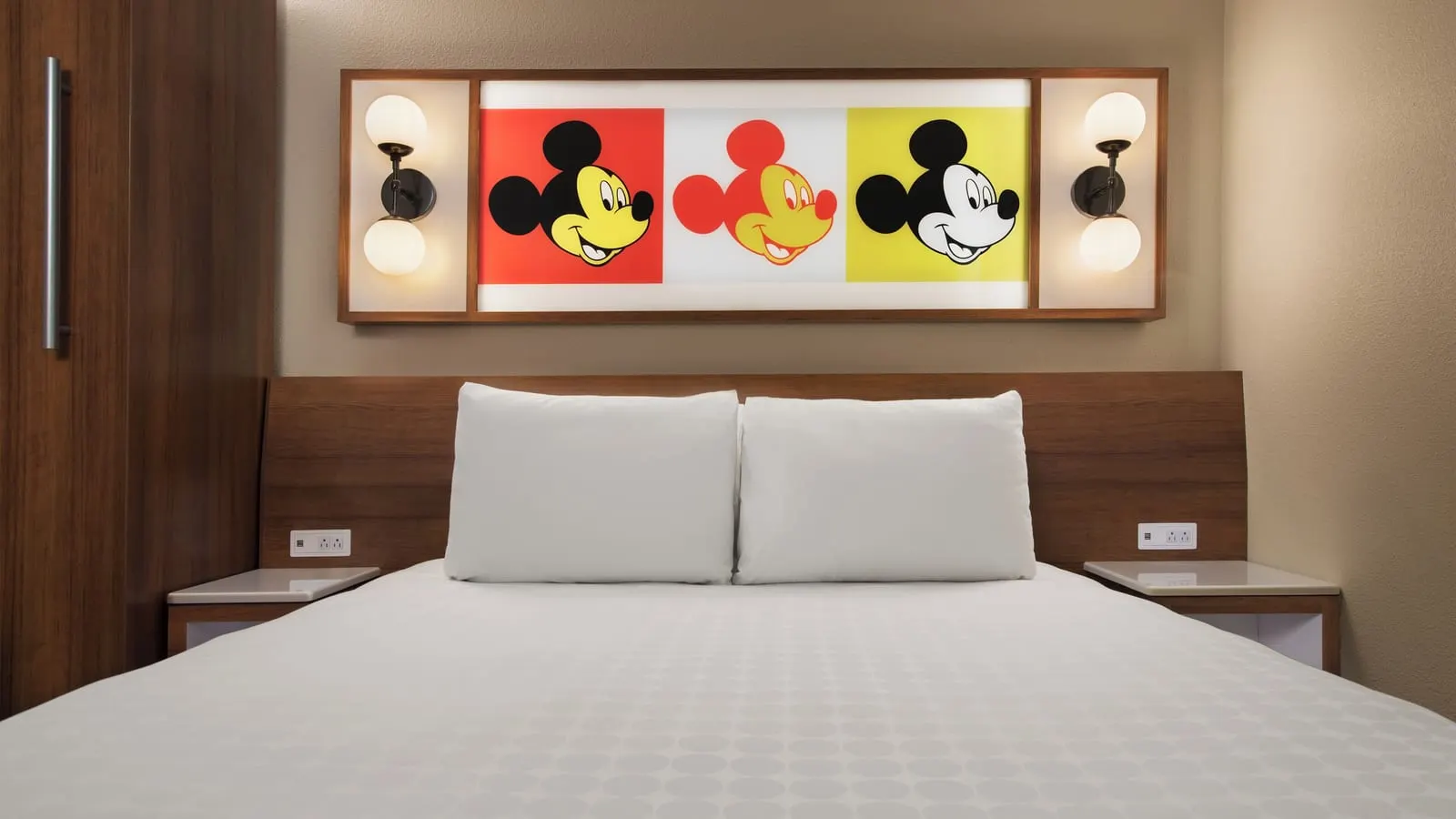 Standard Room at Disney's Pop Century Resort: the queen bed against a wooden headboard, with bedside shelves and a framed triple Mickey Mouse print between two wall lamps