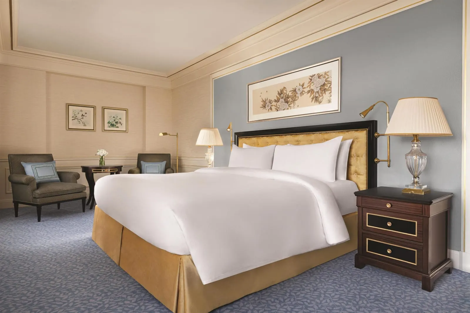 Eiffel View Room at Shangri-La Paris: a king bed with a padded gold headboard against a blue wall, crystal bedside lamps and two armchairs in the corner