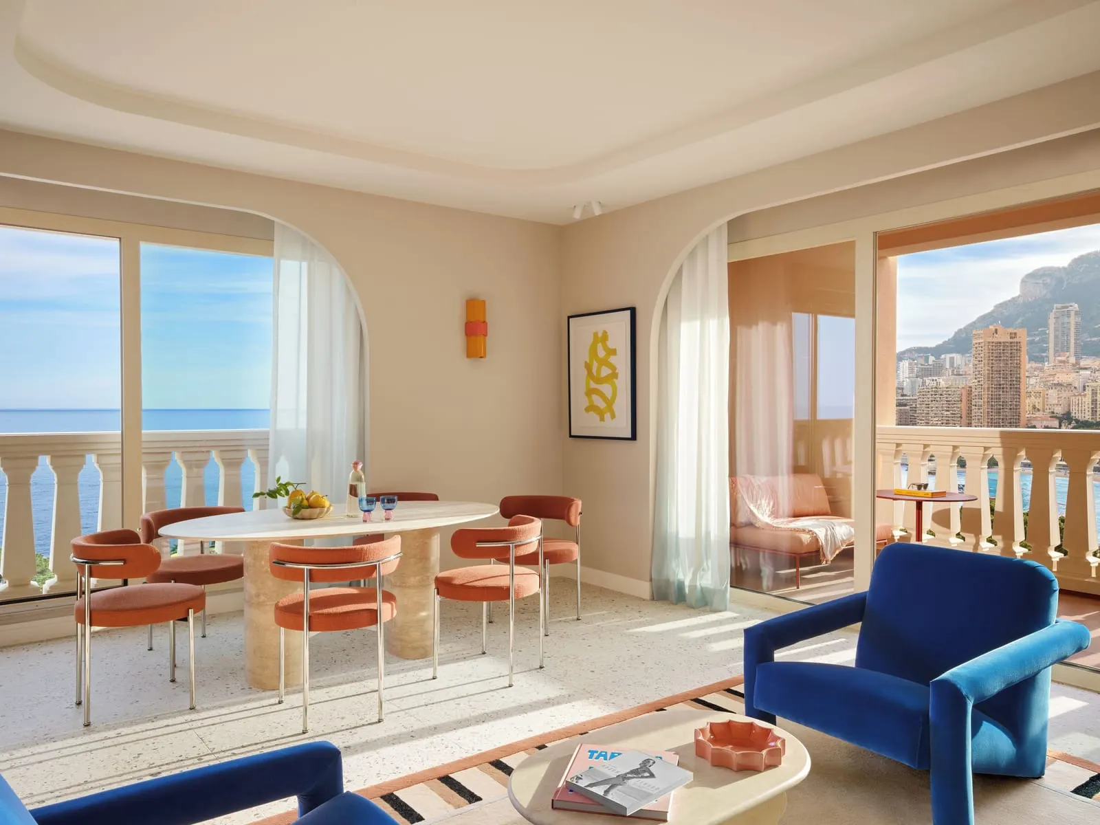 Prestige Superior Suite with sea view at Monte-Carlo Bay Hotel & Resort: an oval dining table and a blue armchair by windows onto the sea