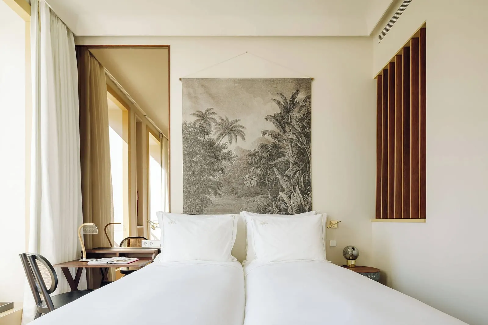 Capelo Twin at The Ivens: two single beds under a palm tapestry, with a desk and chair beside them