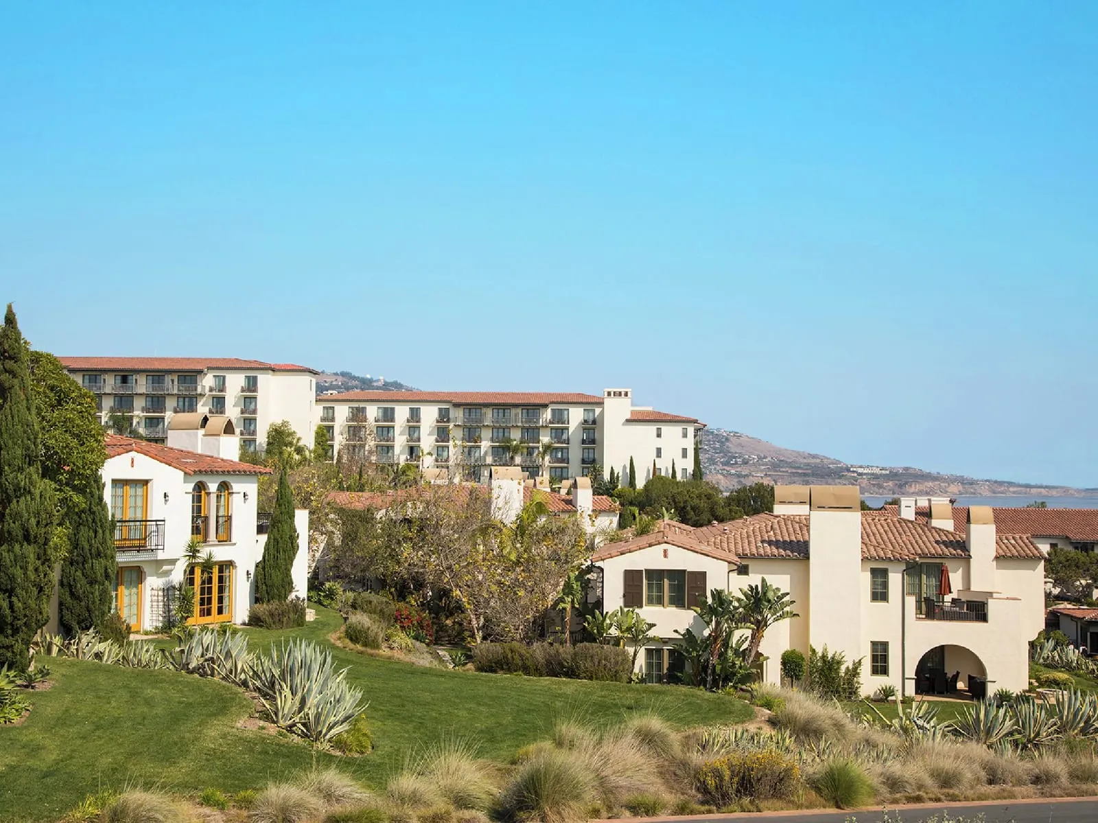 Bungalow King Guestroom at Terranea Resort: white Spanish-style buildings with tiled roofs set among lawn and agave plants, with the main hotel building rising behind