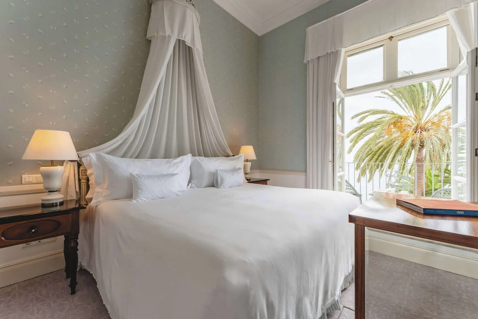 Atlantica Suite at Reid's Palace, A Belmond Hotel: a bed under a white canopy beside tall windows open to palm trees