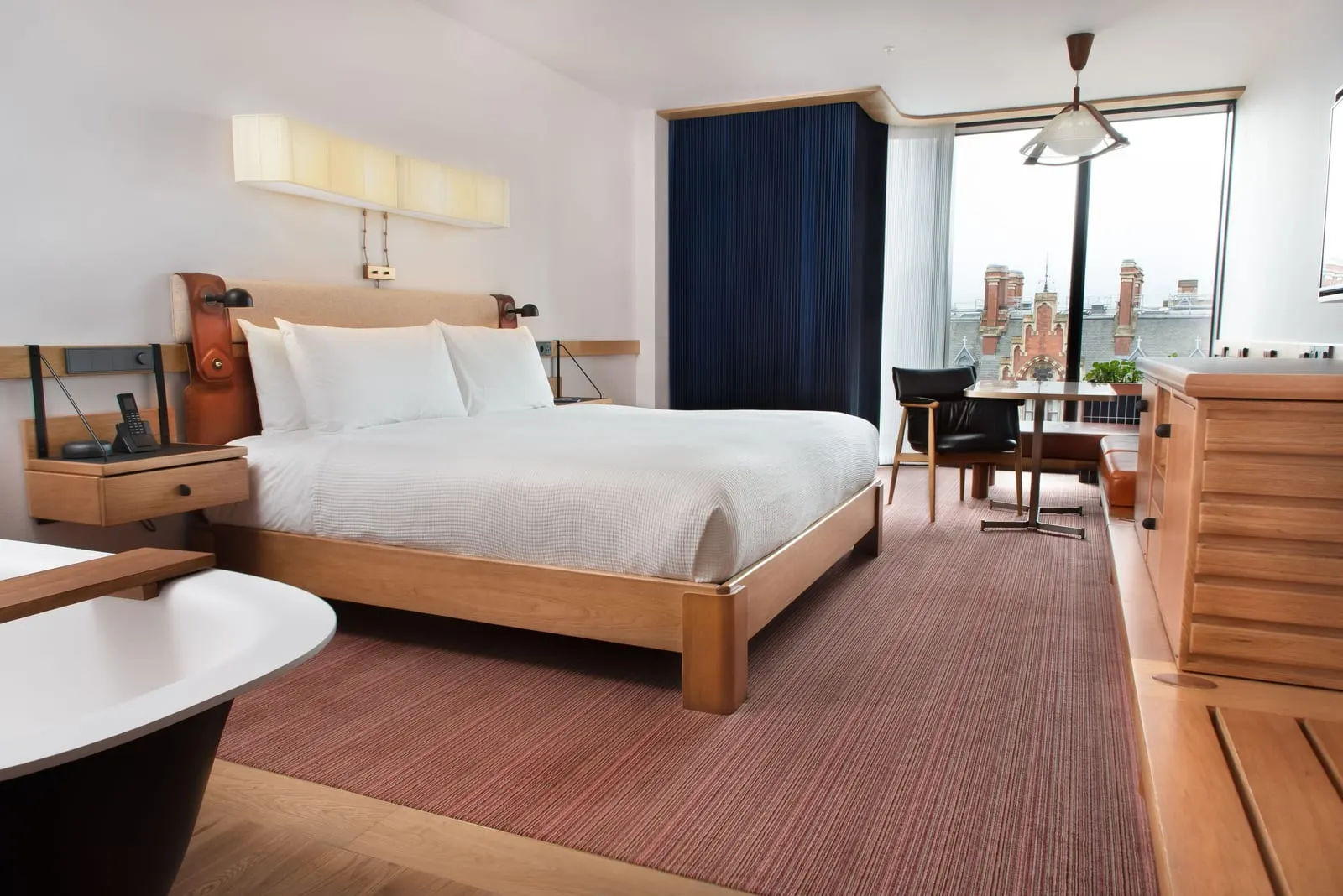Studio Suite at The Standard, London: the bed, a black freestanding bath and a table with chairs by floor-to-ceiling windows