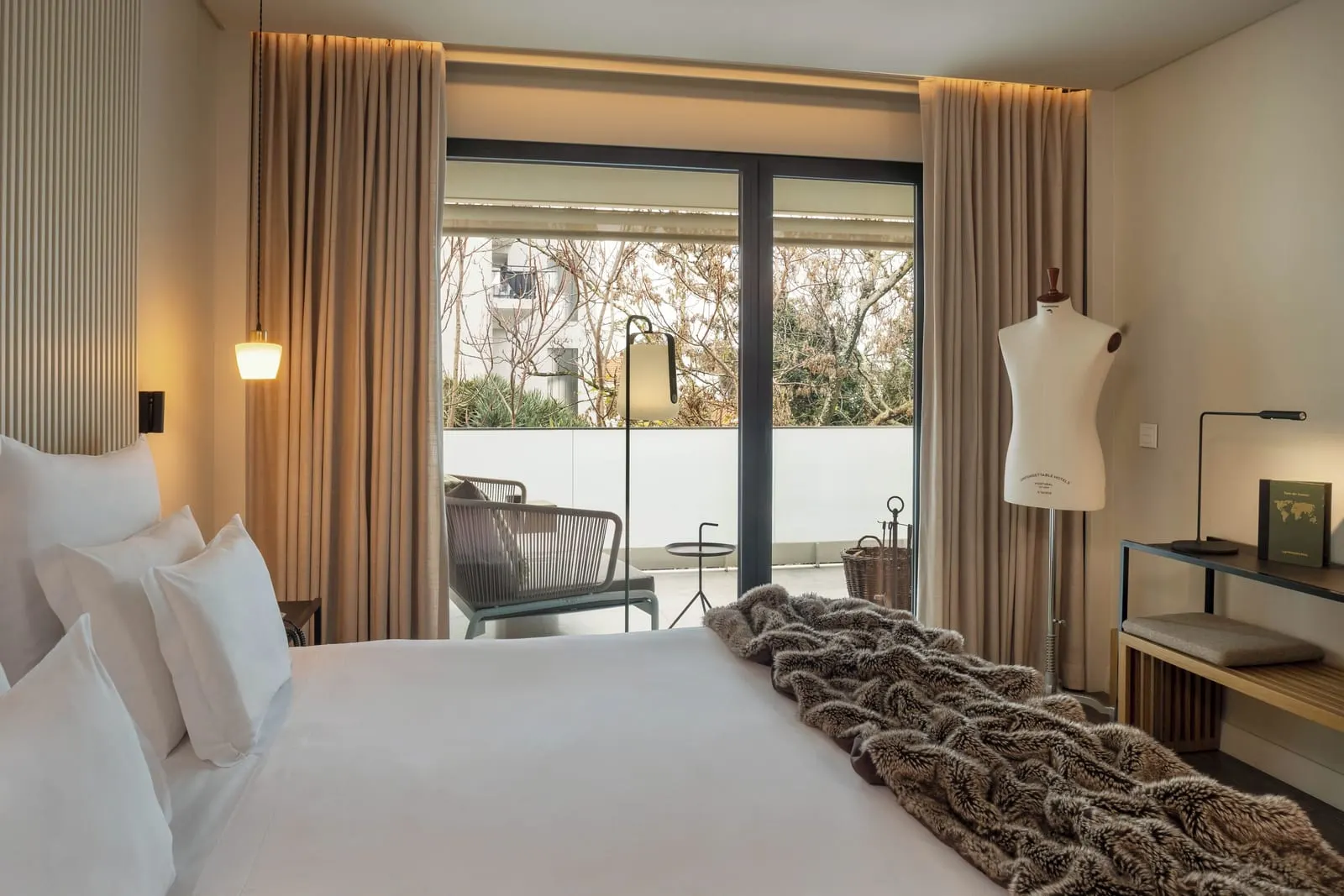Exclusive Room at Memmo Príncipe Real: the bed and glass doors to a balcony with a woven lounge chair and a floor lamp