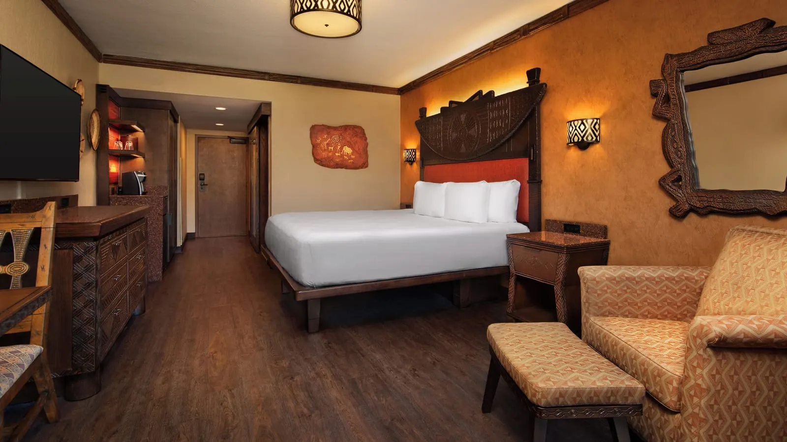 Water View King Bed room at Disney's Animal Kingdom Lodge: a king bed with a carved wooden headboard, an armchair and footstool, a chest of drawers and a coffee station by the door