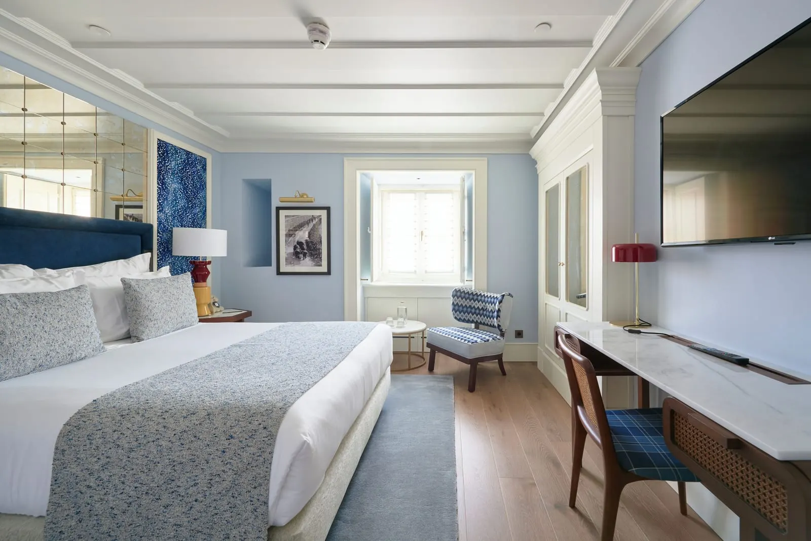 Comfort Room at Palácio Ludovice: the bed with a navy headboard, a desk under a wall-mounted TV and a window at the end