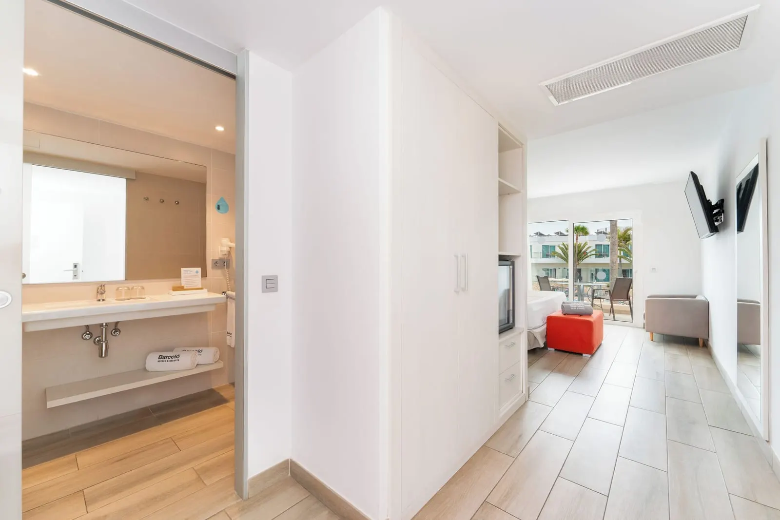 Suite Pool View at Barceló Corralejo Sands: the entrance hall with the bathroom basin on one side and a wardrobe leading through to the bedroom and terrace.