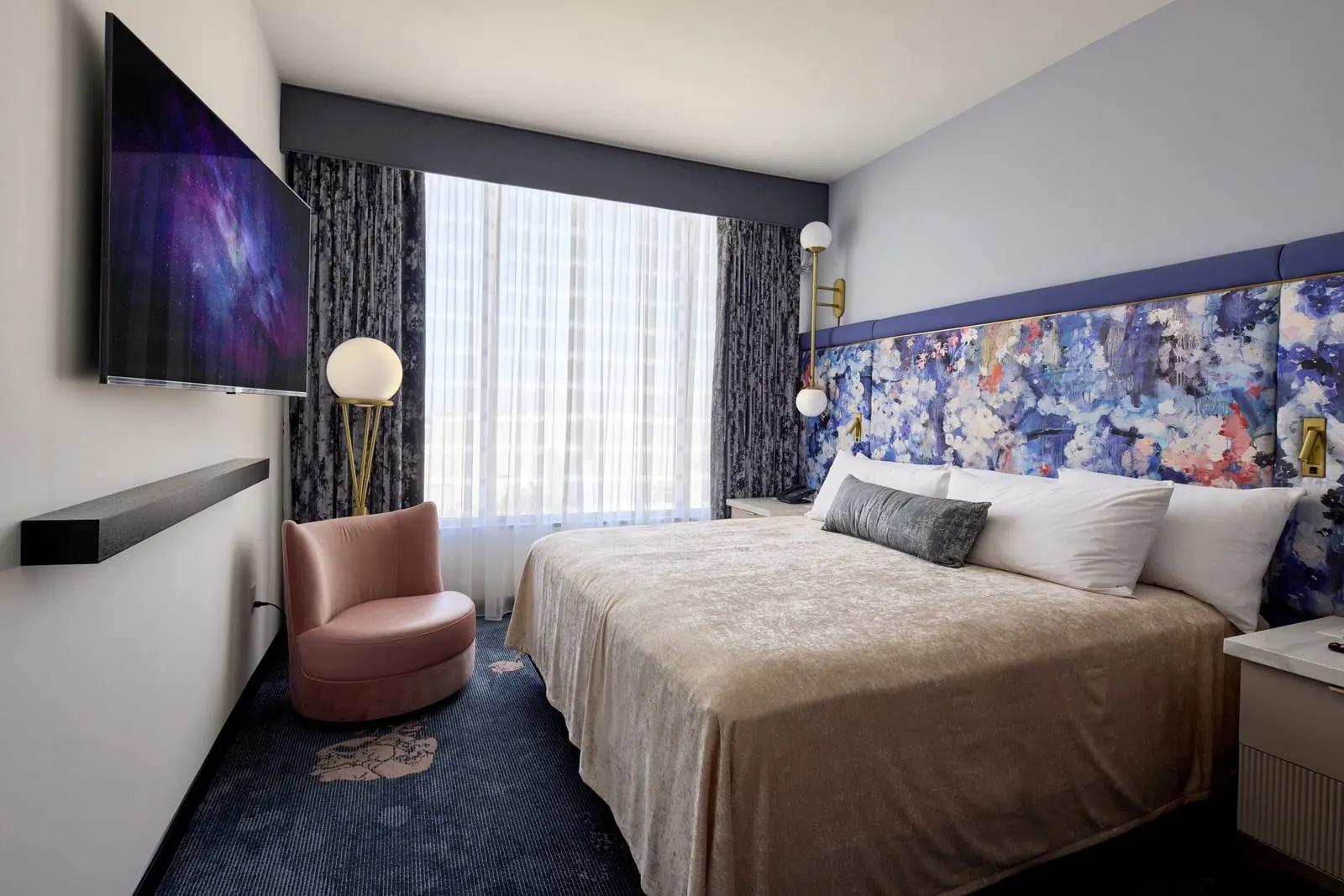 Park View How To Train Your Dragon Kids' Suite at Universal Helios Grand Hotel: the main bedroom, with a king bed against a floral headboard, a pink armchair by the window and a wall-mounted television