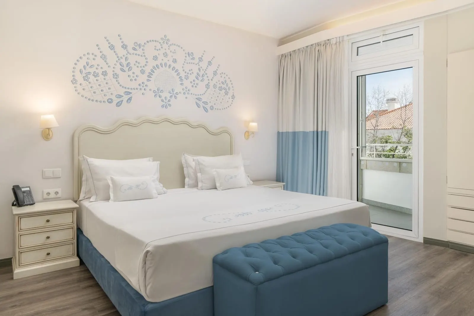 Superior Suite im Hotel Madeira: ein großes Doppelbett mit einer blau gepolsterten Bank am Fußende und einer Glastür zum Balkon