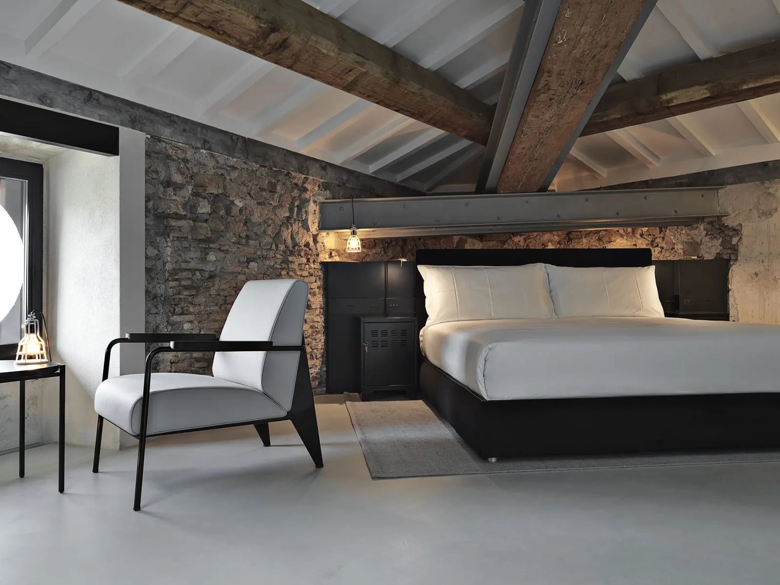 Deluxe Double Apartment at Rhinoceros Roma: the bed under timber roof beams, with an armchair and a stone wall