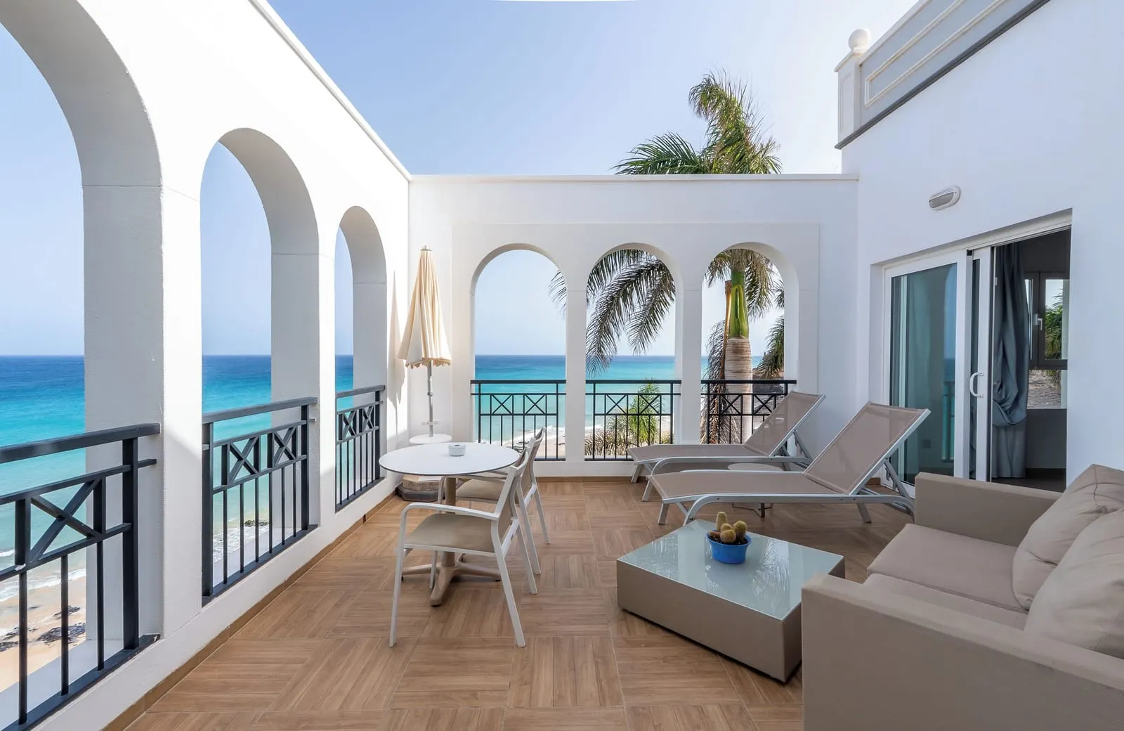 Royal Suite at Royal Palm Resort & Spa: a terrace with arched walls, a sofa, a coffee table, sun loungers and a dining table, with the sea beyond the railings