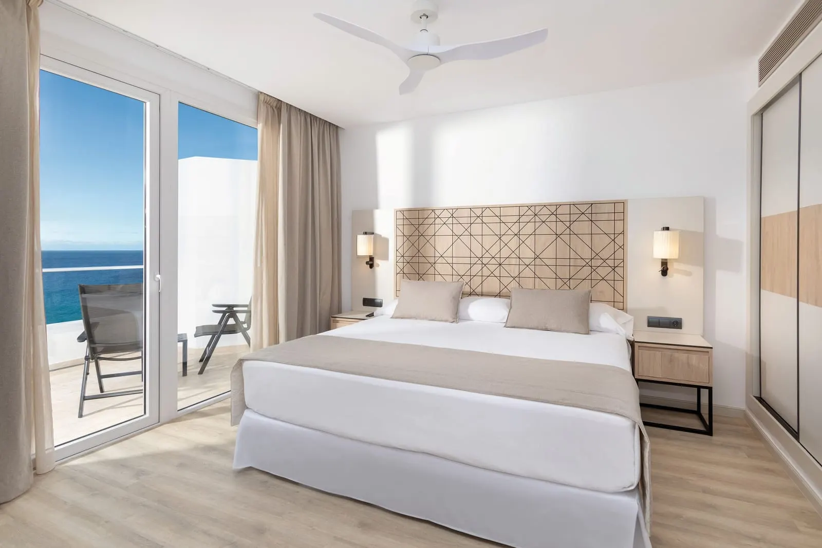 Suite Senior (2 Bedrooms) with sea view à l'Hotel Riu Palace Jandía : un lit sous une tête de lit en treillis de bois près d'une porte de balcon ouverte sur la mer