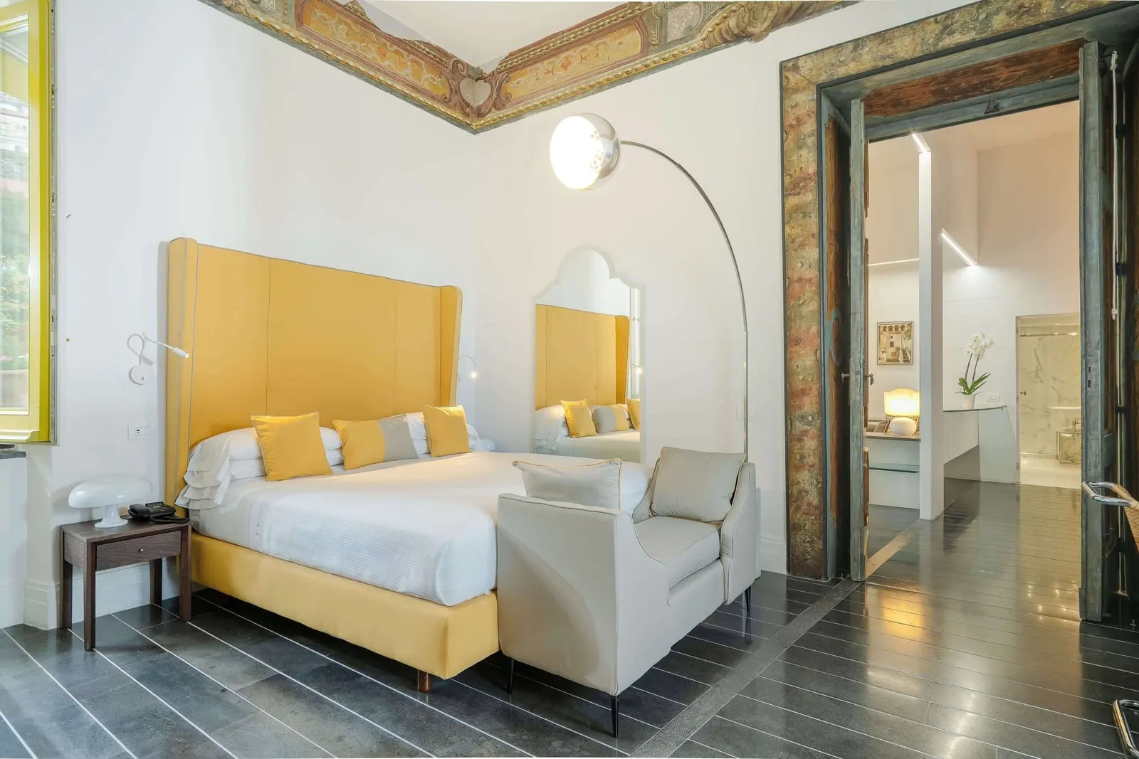 Superior Suite im Palazzo Murat: ein Doppelbett mit hohem gelbem Kopfteil unter einer bemalten Deckenbordüre, mit dem Bad dahinter