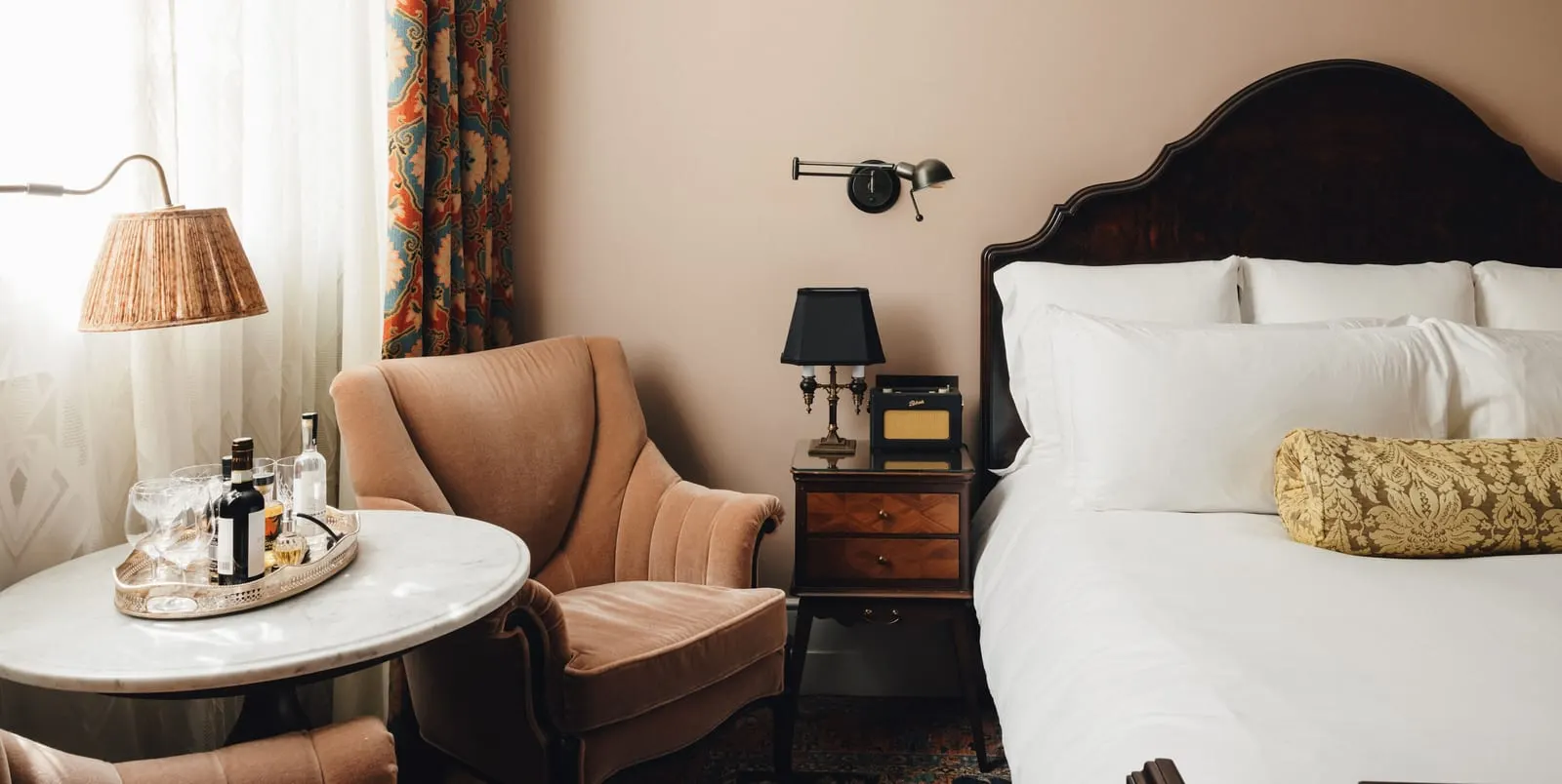 Medium room at The Ned: the bed with a carved headboard, a velvet armchair and a round marble table with a drinks tray