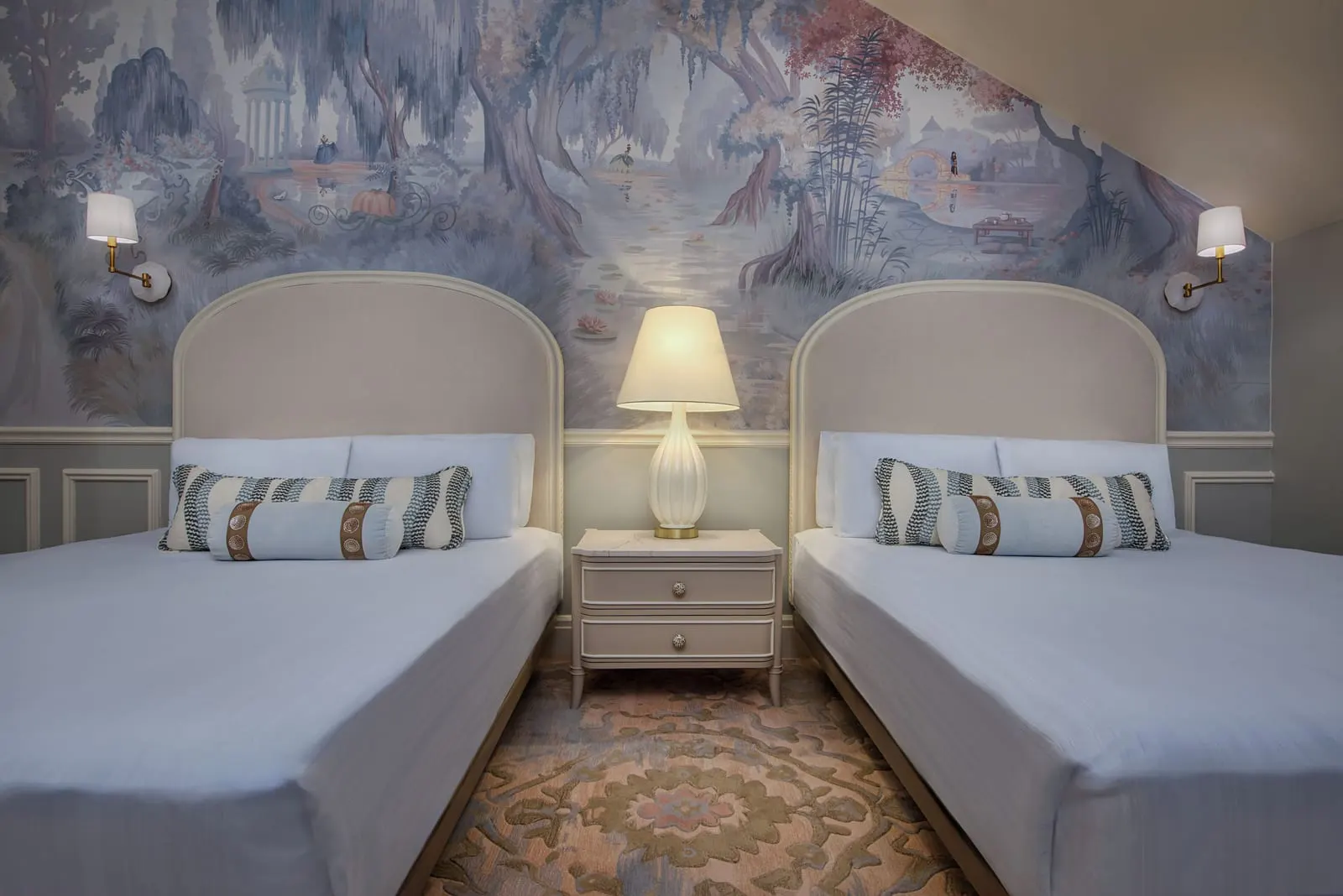 Resort View room at Disney's Grand Floridian Resort & Spa: two queen beds with arched cream headboards in front of a painted landscape mural, with a lamp on the bedside table between them