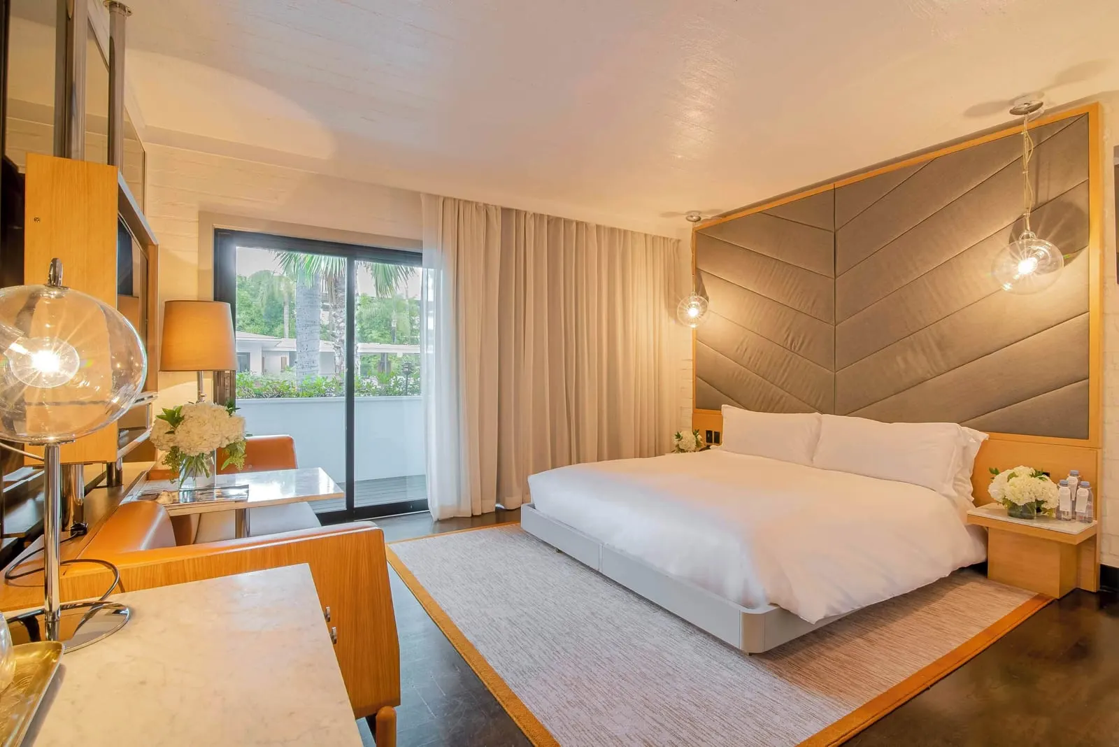 Cabana Balcony King im The Hollywood Roosevelt: ein Kingsize-Bett vor einem Kopfteil aus Chevron-Paneelen, mit einer Sitzecke aus Leder und Marmor und gläsernen Schiebetüren daneben