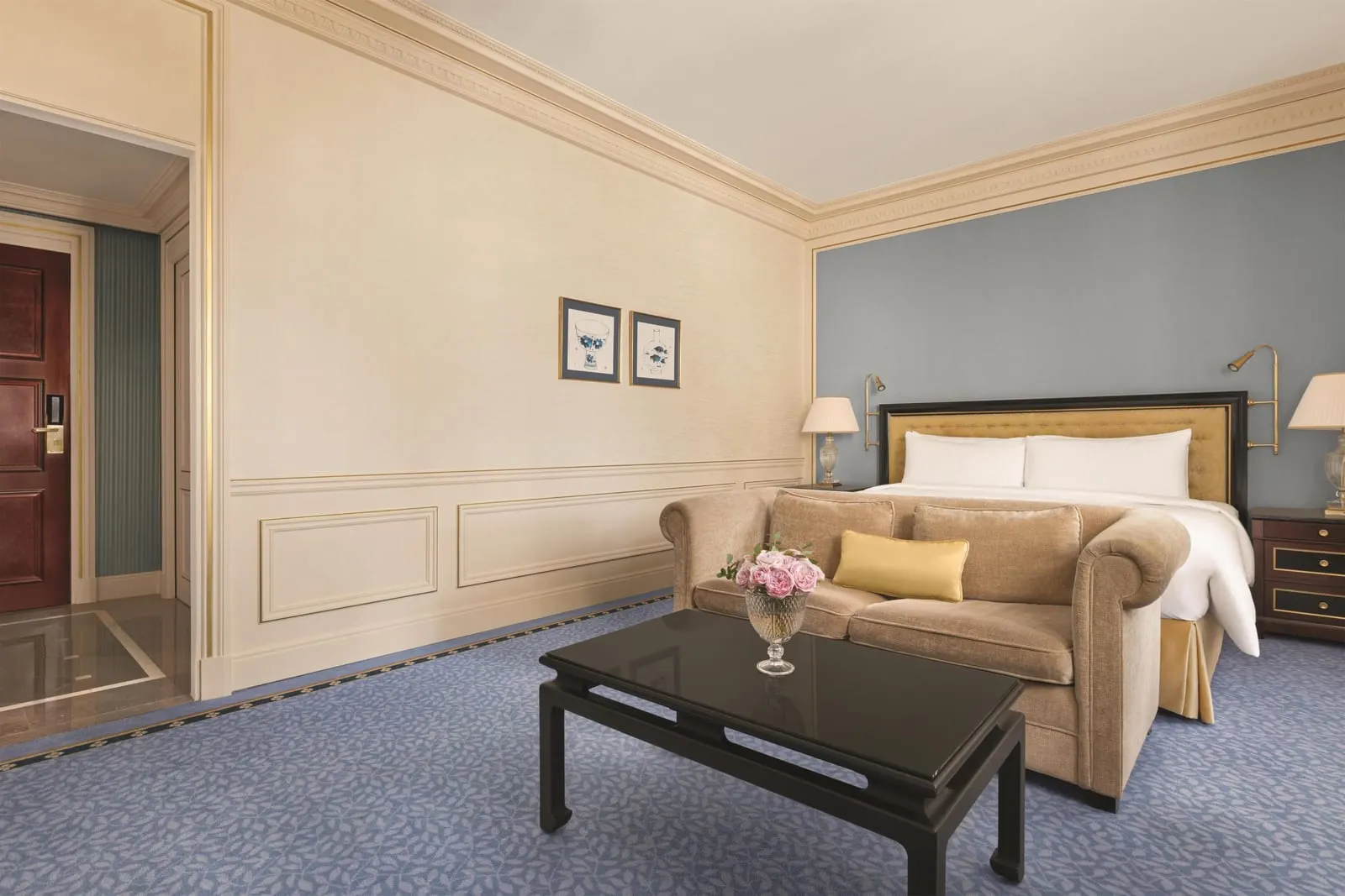 Superior Room at Shangri-La Paris: a king bed with a padded gold headboard against a blue wall, a velvet sofa at its foot and a black lacquered coffee table, with the entrance hall to the left