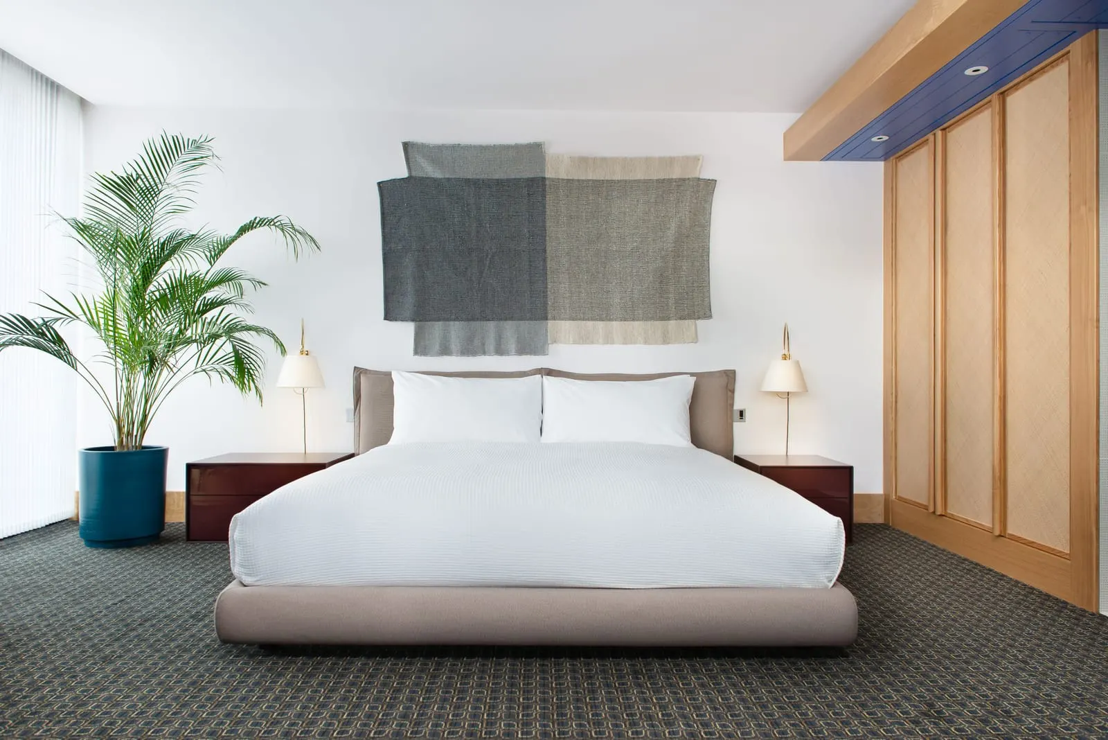 Suite Spot at The Standard, London: the bed below a woven wall hanging, with a palm and wood-panelled wardrobes