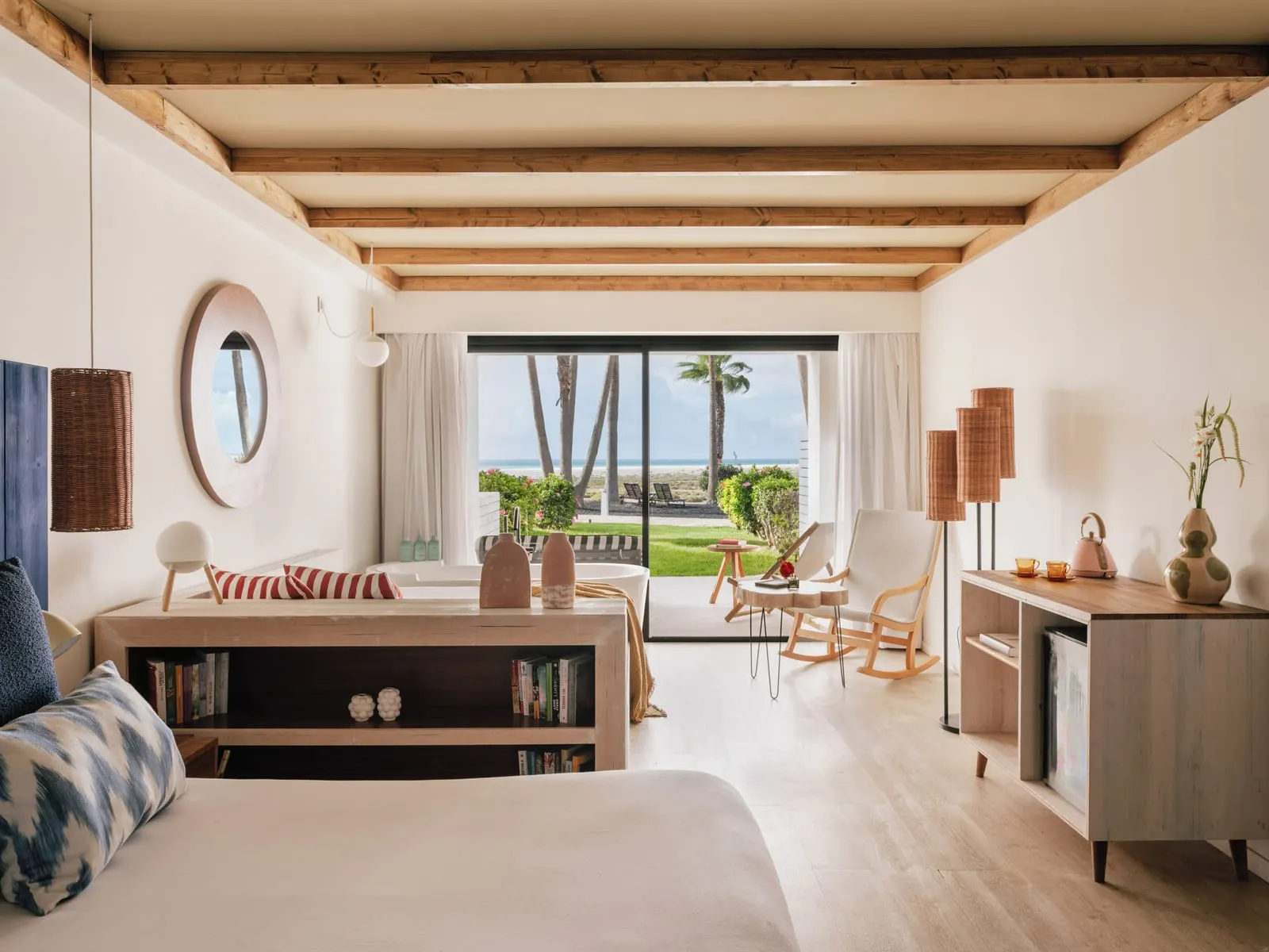 Zel Suite Ocean View with Garden at ZEL Fuerteventura: a bed facing a low bookcase and a seating area by a glass wall onto a terrace and lawn