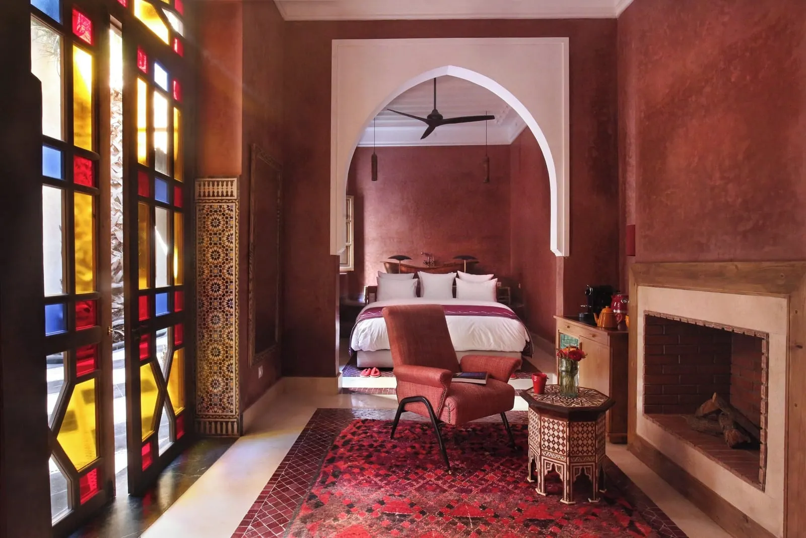 Medium Room at El Fenn: a bed beyond a carved arch, with an armchair and side table beside an open fireplace and stained-glass windows