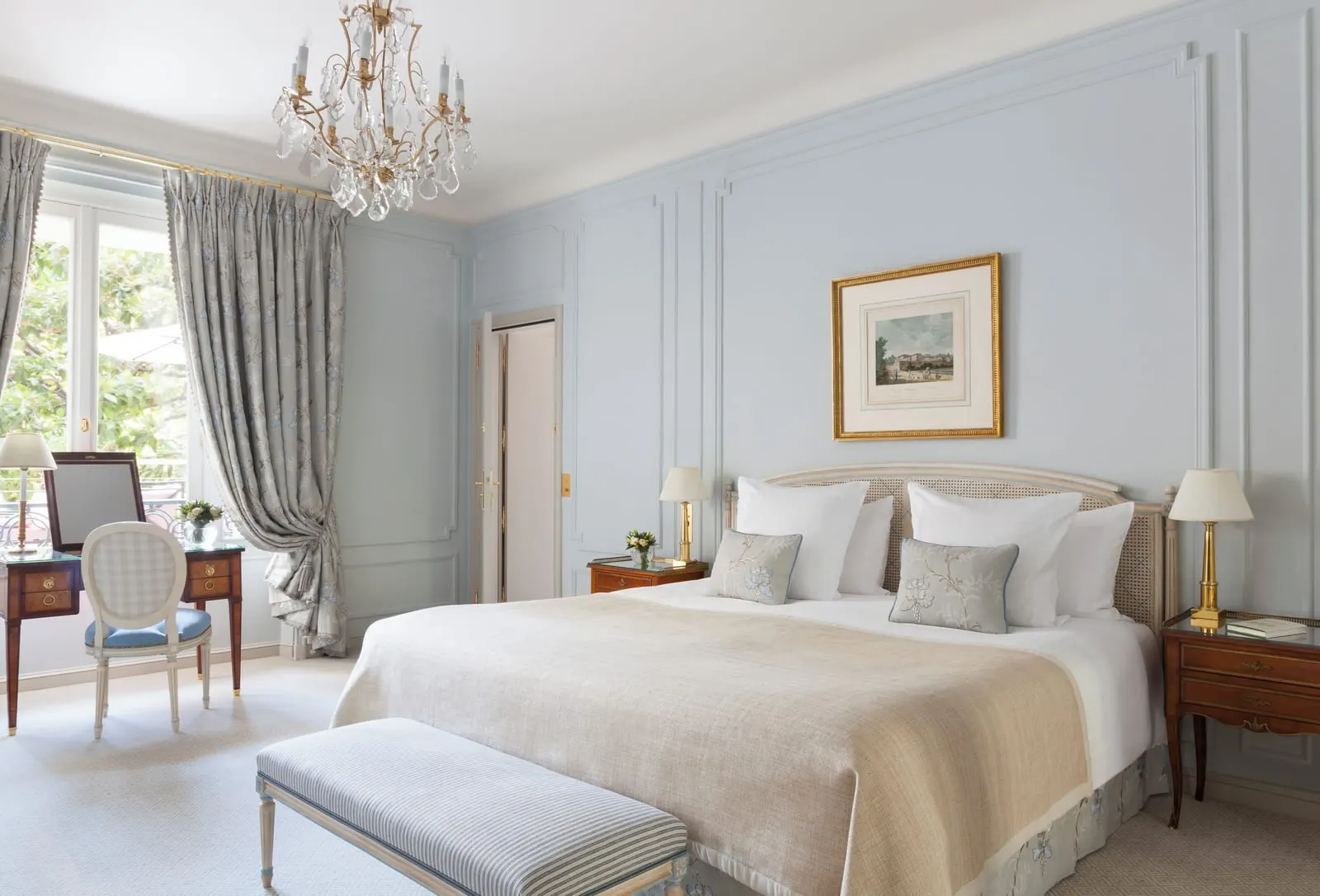 Suite Magnolia at Le Bristol Paris: a bed with a sand-coloured throw against pale blue panelled walls, with a dressing table by a tall window