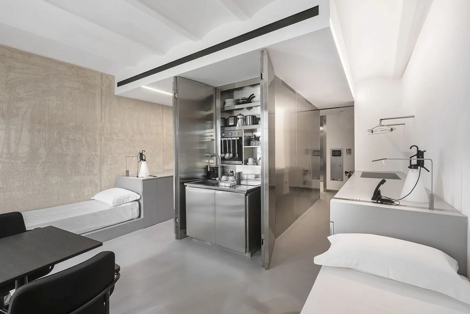Studio Apartment at Rhinoceros Roma: two beds either side of a steel kitchen unit, with a table and chair