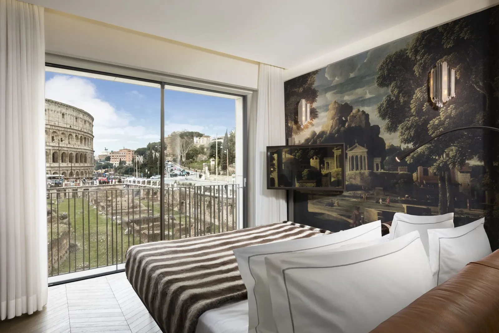 Grand View J Suite at Palazzo Manfredi: the bed below a landscape mural and a glass wall onto the Colosseum