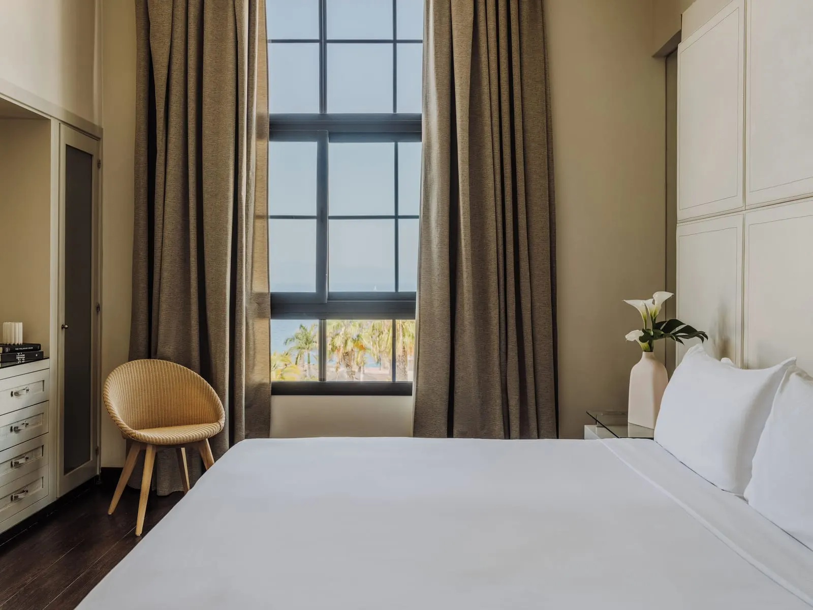 RedLevel Suite Ocean View at Gran Meliá Palacio de Isora: the bedroom, a wicker chair and a tall window onto palms