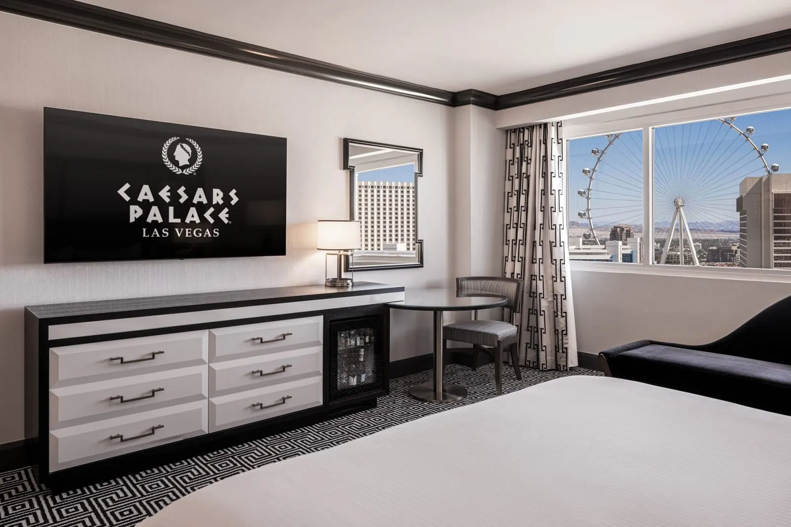 Colosseum Strip View Room im Caesars Palace: eine weiße Kommode unter einem wandmontierten Fernseher, ein kleiner runder Tisch mit Stuhl, eine Chaiselongue und ein Fenster