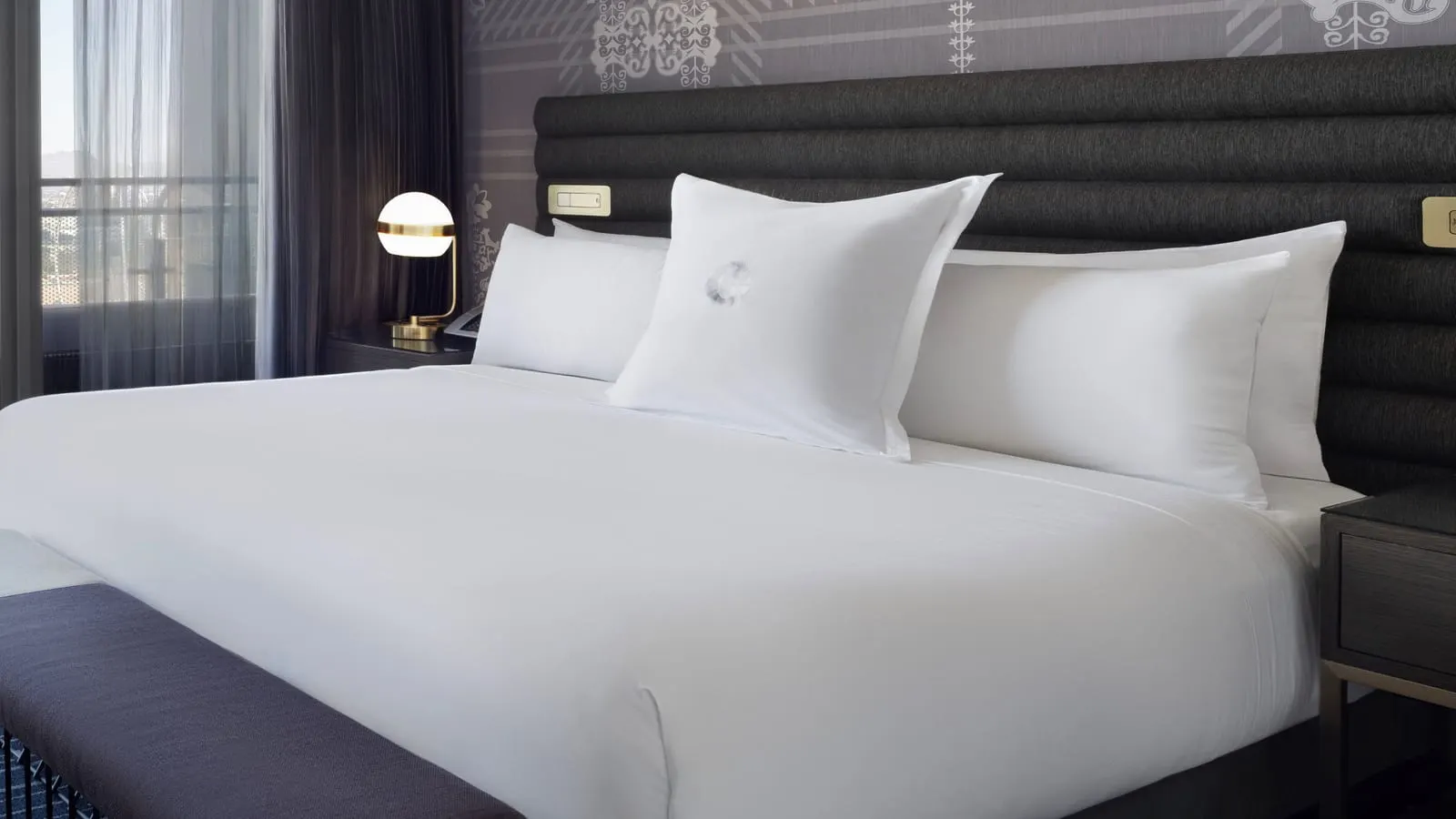 Terrace Studio King at The Cosmopolitan of Las Vegas: a king bed with a padded charcoal headboard, a brass globe lamp on the bedside table and a long upholstered bench at its foot