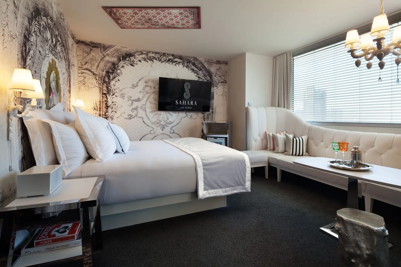 Alexandria King at SAHARA Las Vegas: a king bed against a black and white baroque-print wall, a white tufted banquette curving along the window, a white table and a wall-mounted TV