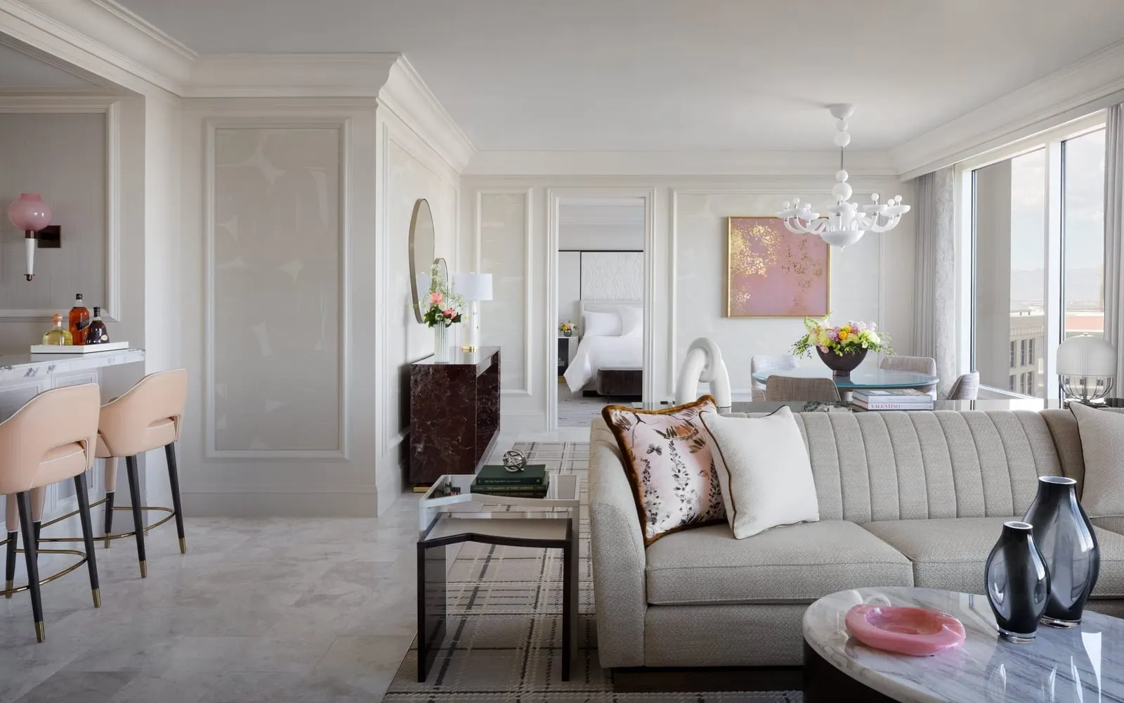 Penthouse Suite at Bellagio: the living room, with a long sofa, a bar area with stools, a dining table under a white chandelier and the bedroom through an open door