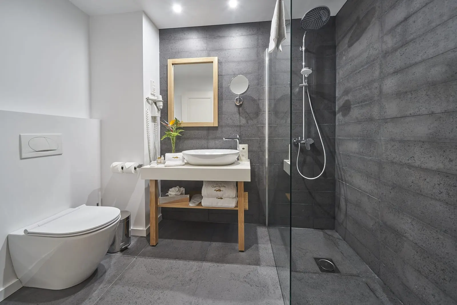 Premium Room im Hotel Quinta do Furão: ein Bad mit grauen Steinfliesen, einer begehbaren Dusche hinter einer Glaswand, einem Aufsatzwaschbecken auf einem Holzgestell und einem wandhängenden WC