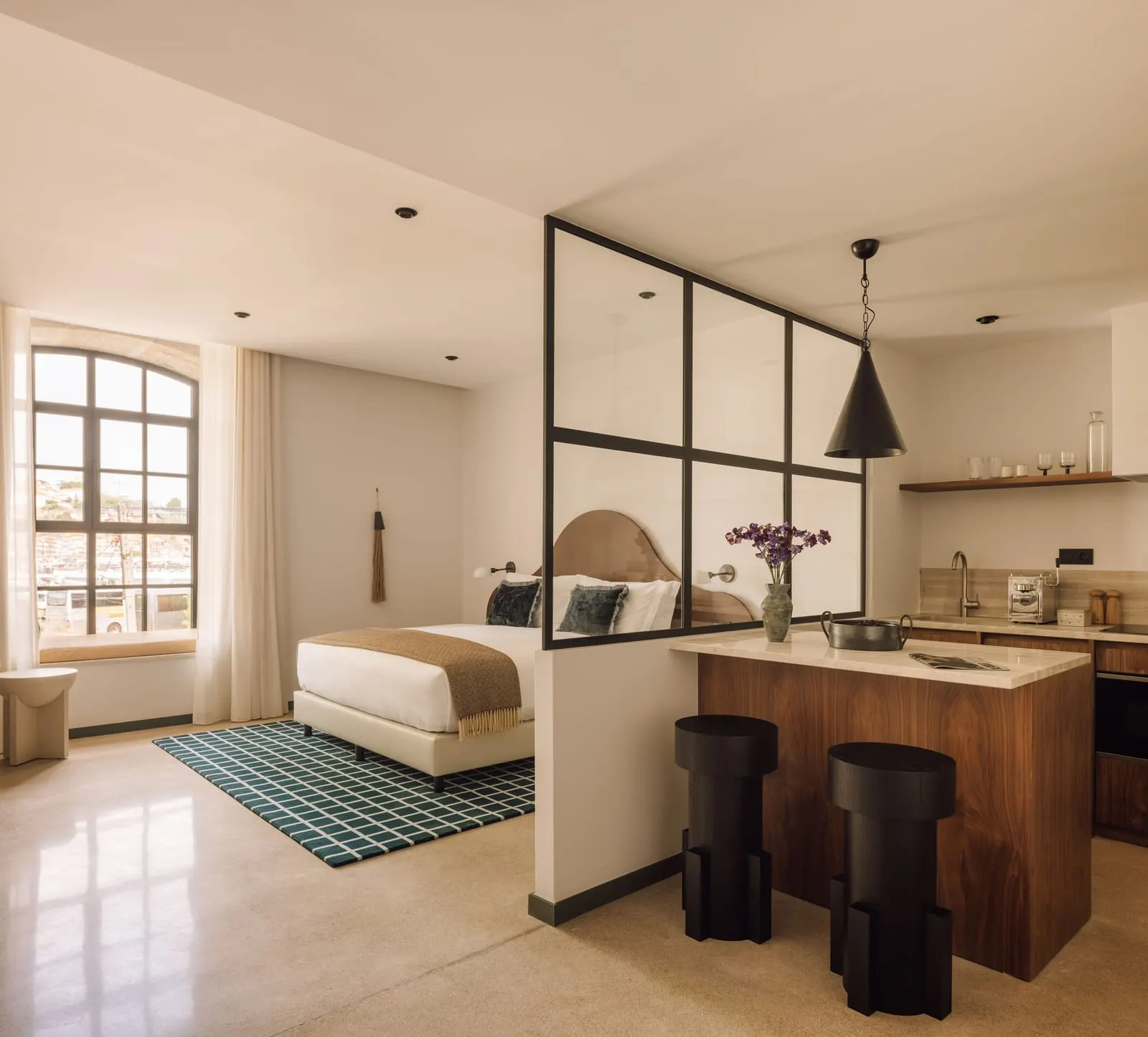 River Studio at The Rebello: the bed behind a glass partition, a kitchen island with stools and an arched window