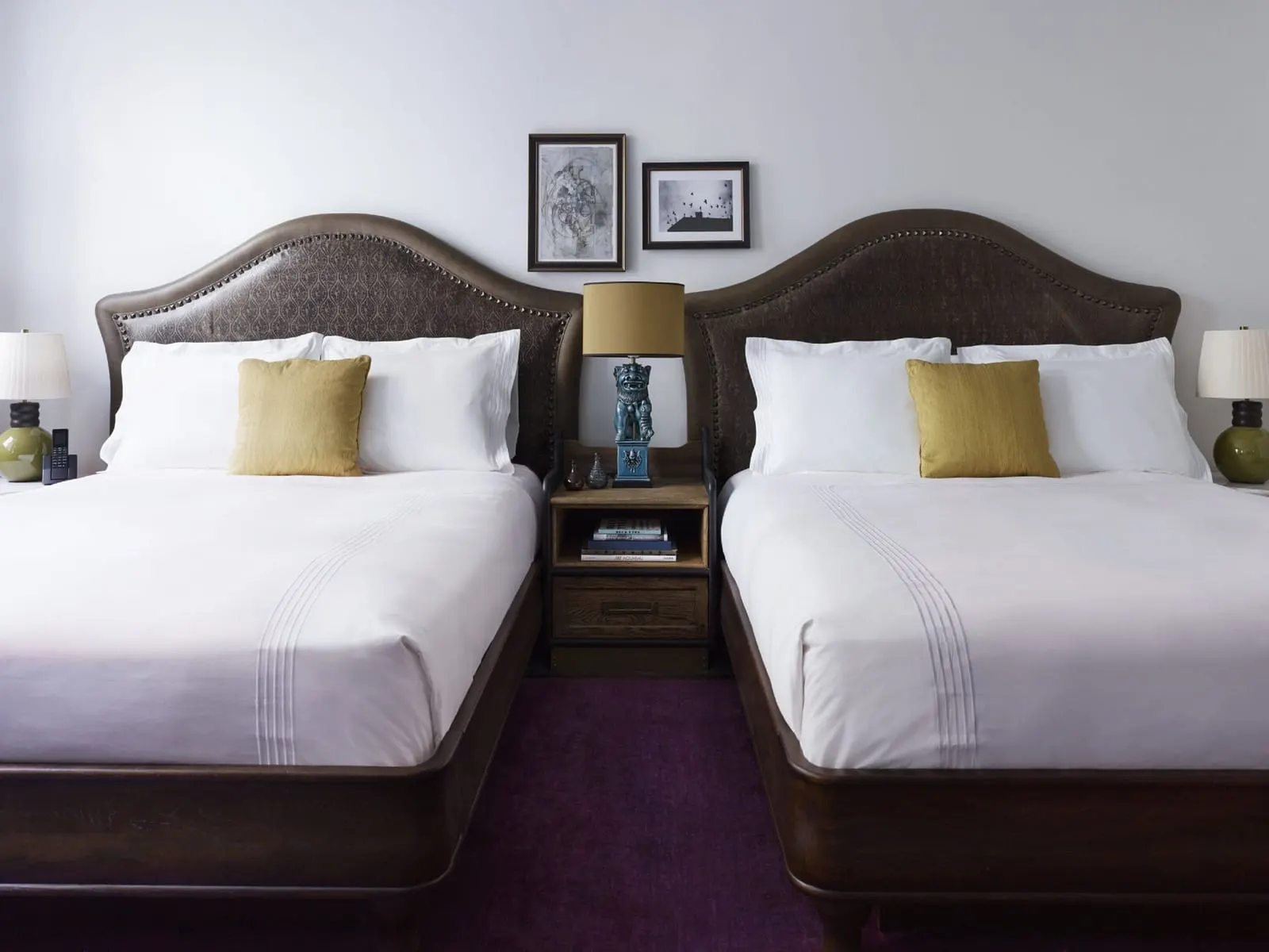 Double Queen at The Beekman: two queen beds with studded leather headboards and white linen, a wooden bedside table and a lamp between them
