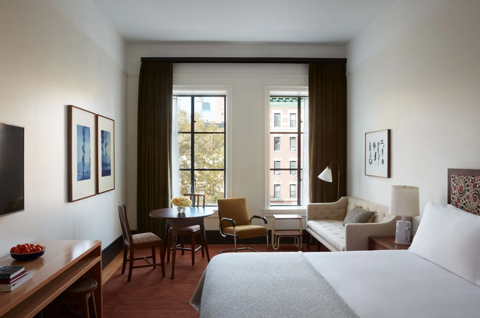 Classic King at Nine Orchard: a bed with a grey throw in a bright room with two black-framed windows, a round dining table and chairs, a sofa and a wooden desk