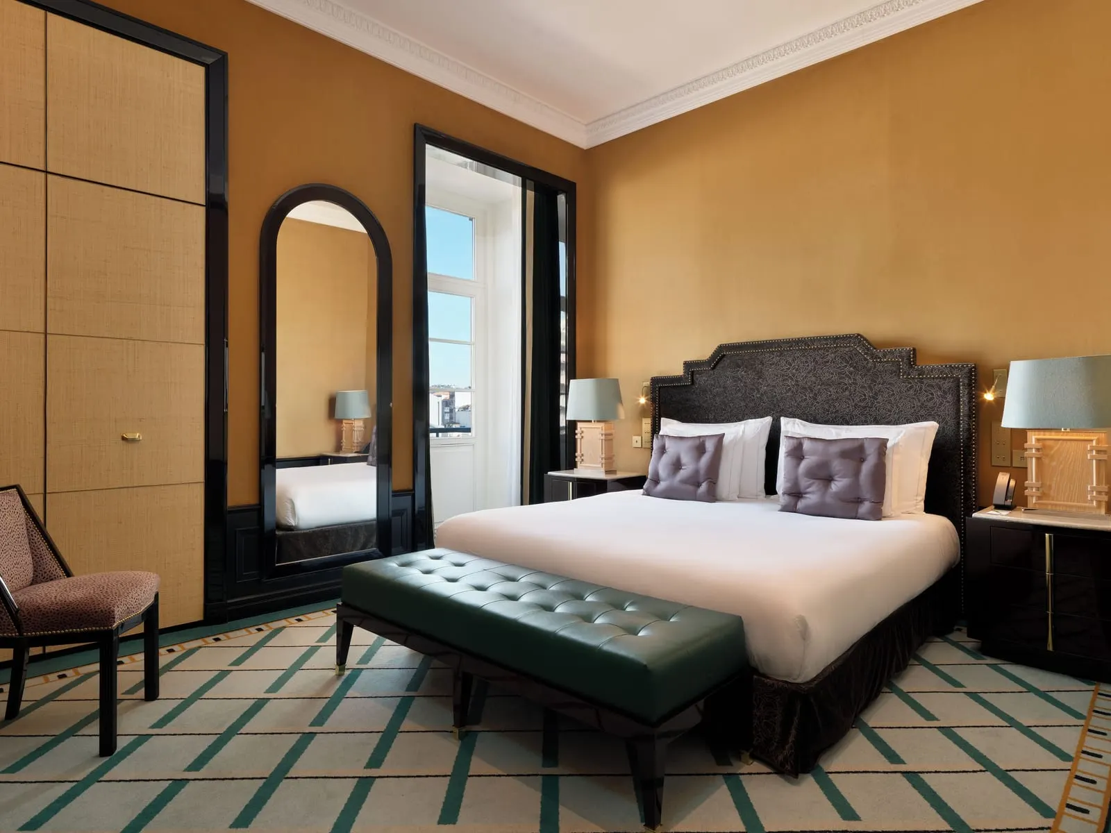 Monumental Suite bedroom at The One Monumental Palace: the bed with a leather bench, an arched mirror and a tall window
