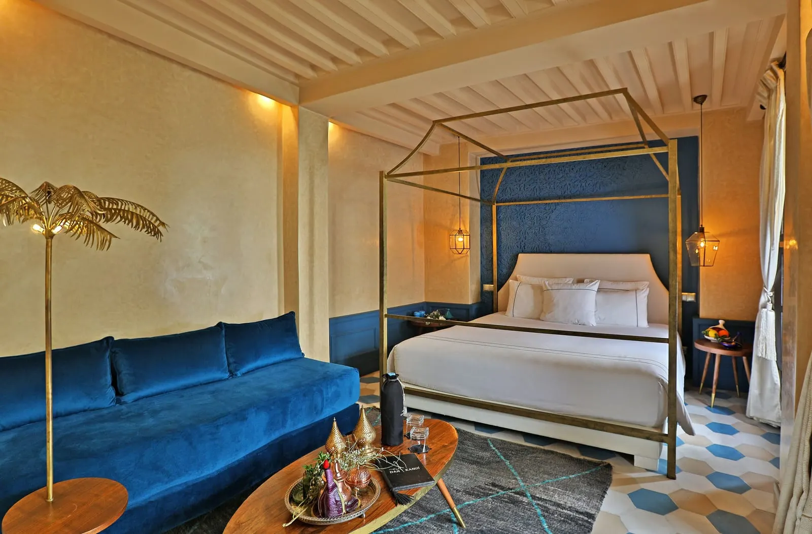 Suite Balcony at Dar Kandi: a canopy bed against a blue headboard wall, with a blue velvet sofa and a low wooden table
