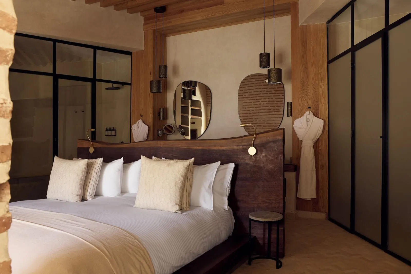 Nobu Riad at Nobu Hotel Marrakech: a bedroom with a timber headboard, pendant lights and a glazed partition to the bathroom
