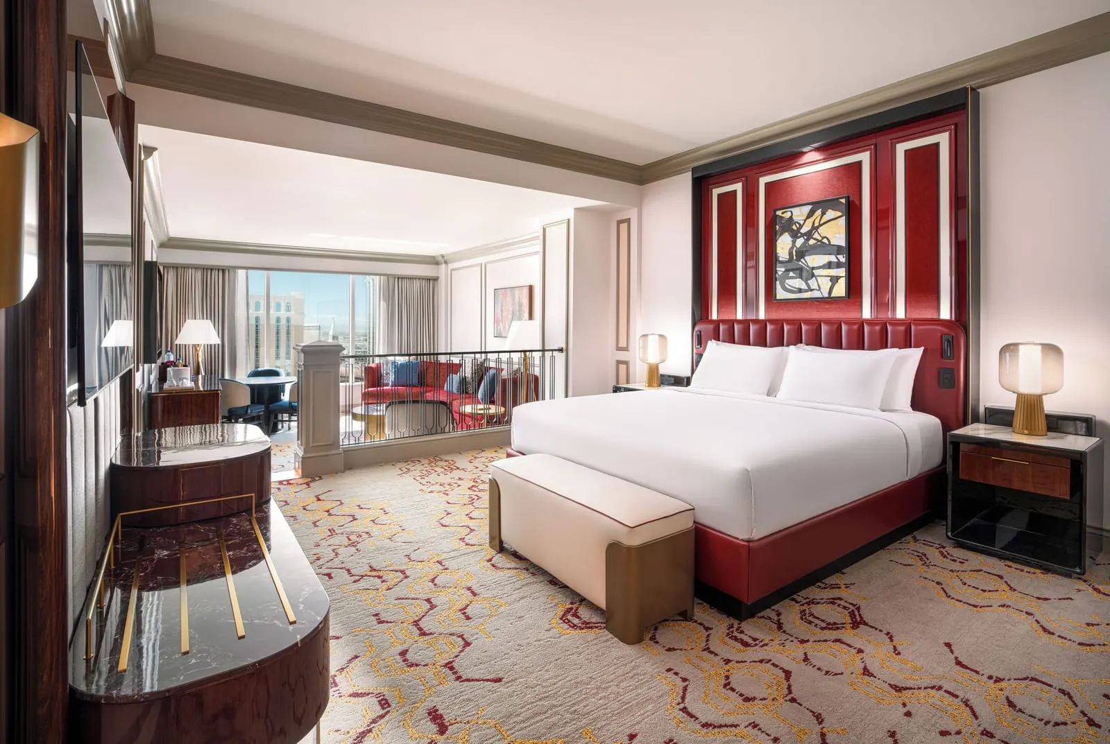 Newly Remodeled Luxury King Suite at The Venetian: a king bed with a red leather headboard and a bench at its foot, and a railing beyond it above a living area with a red sofa
