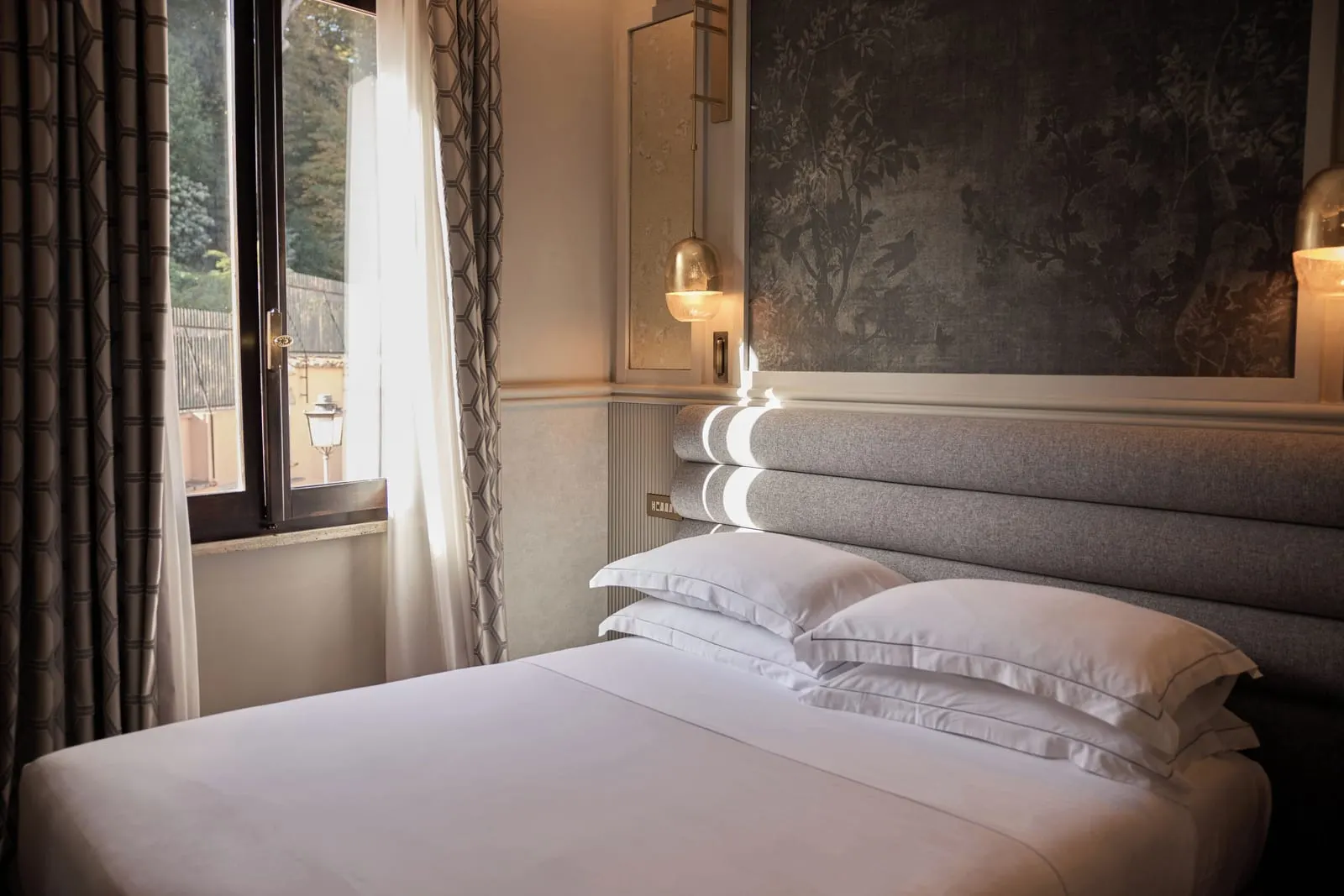 Executive Room at Donna Camilla Savelli: the bed against a padded grey headboard and a painted panel, a window beside it