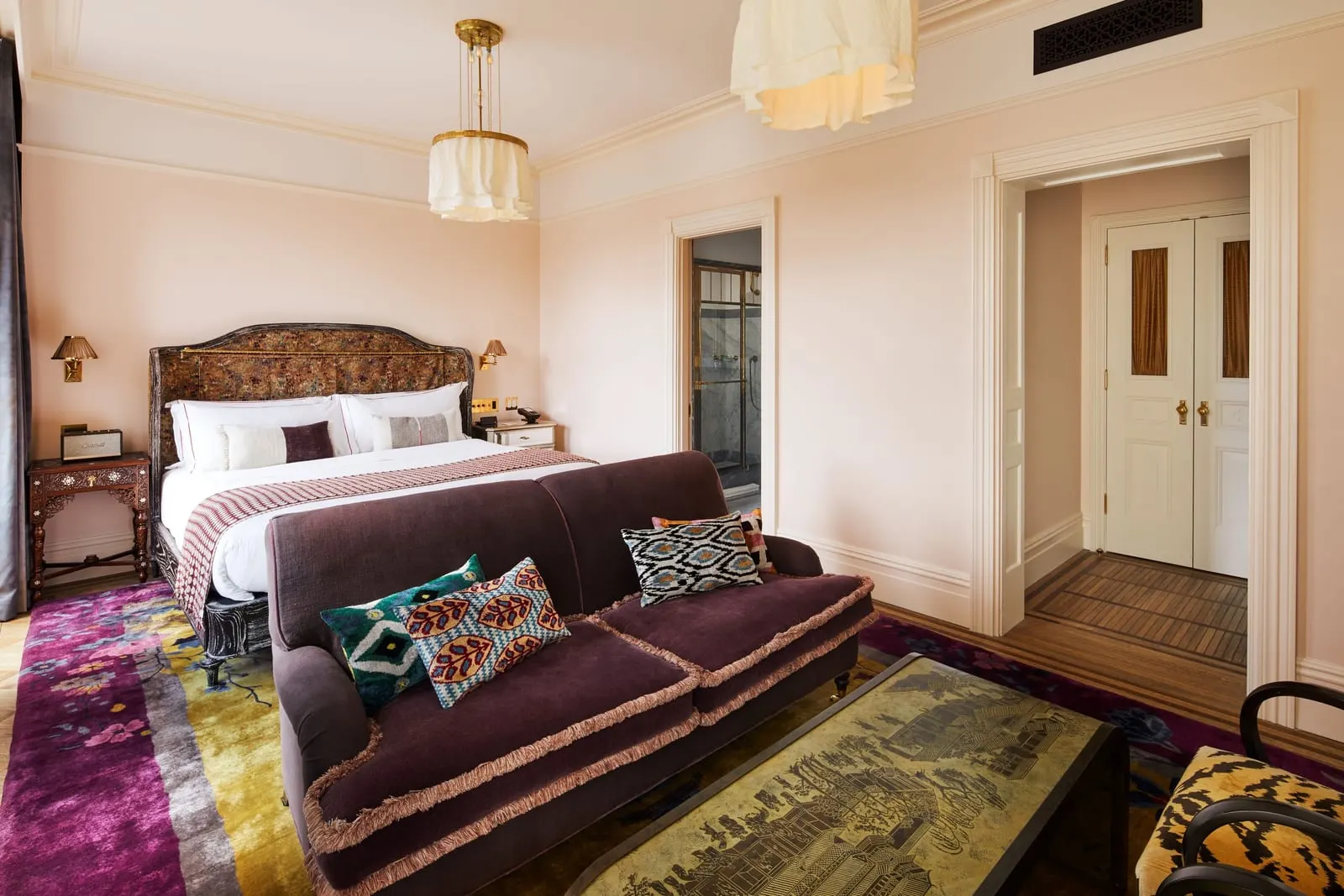 Premier Chelsea at Hotel Chelsea: a bed with a patterned velvet headboard behind a purple sofa and a gilt-patterned coffee table, with a doorway to the marble bathroom