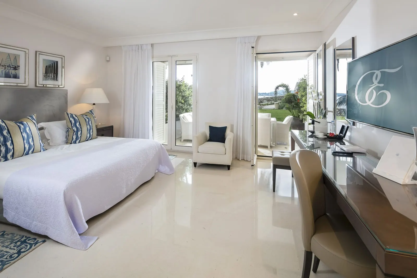 Le Cap Deluxe Room with a sea-view terrace at Cap Estel: the bed, a desk and French windows to the terrace