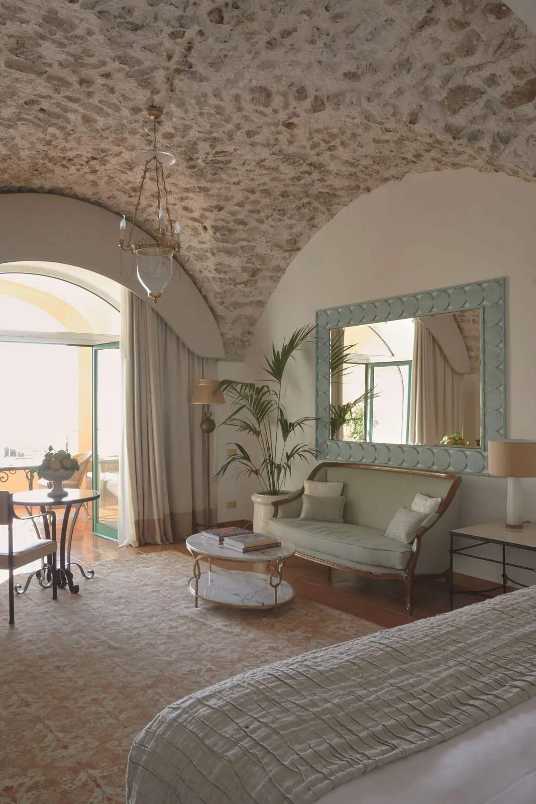 Superior Sea View Junior Suite with Garden at Caruso, A Belmond Hotel: a sitting area with a sofa, a marble coffee table and a small dining table under a vaulted stone ceiling, by glass doors to a terrace