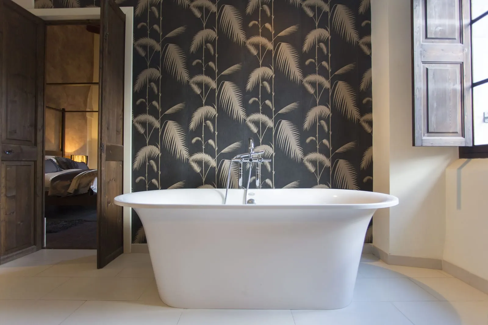Luxury Suite at L'Avenida Hotel: a freestanding white roll-top bath against palm-leaf wallpaper, with the bedroom visible through the open door