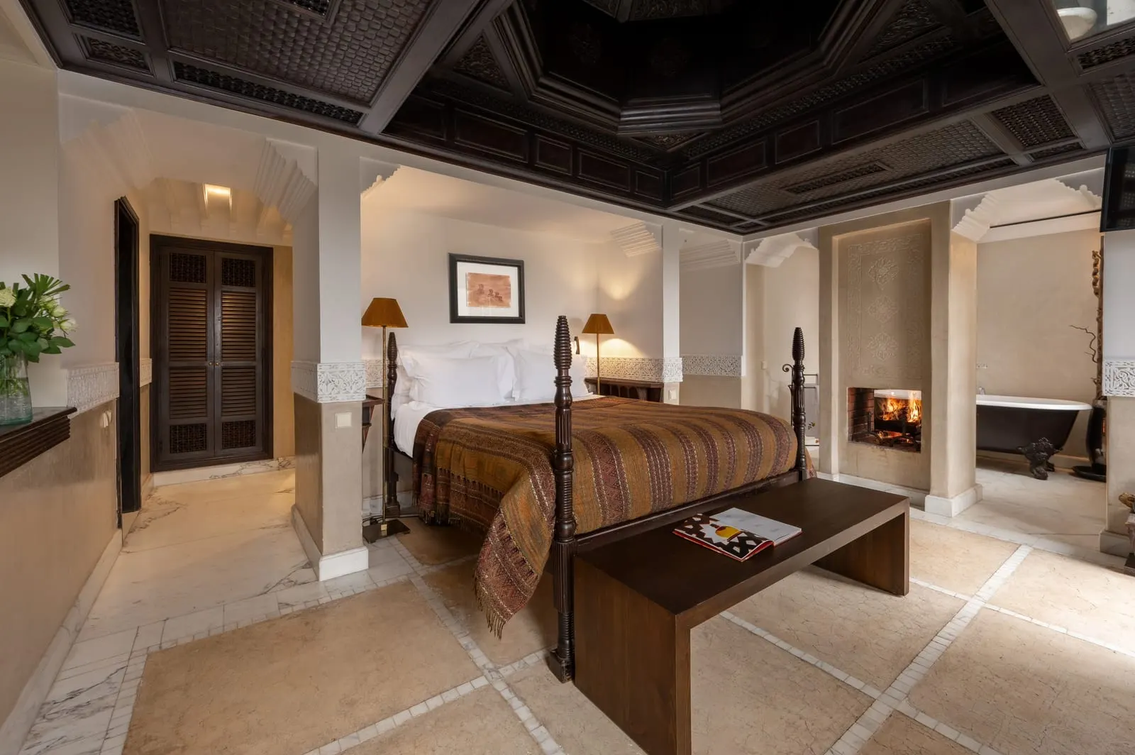 Master Suite at La Villa des Orangers: a four poster bed beneath a carved wooden ceiling, with a fireplace and a freestanding bath beyond.