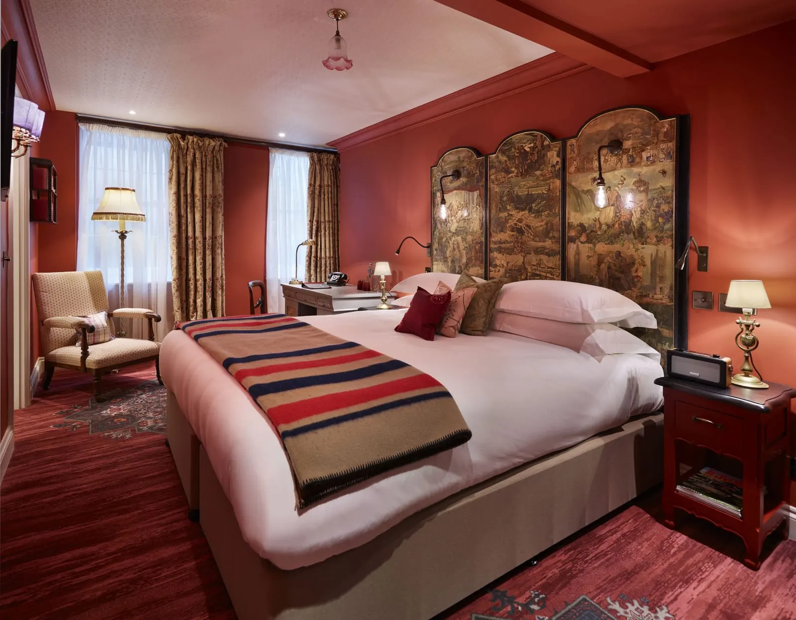 Deluxe King at The Zetter Marylebone: the bed with a painted screen headboard, red walls, an armchair and two windows